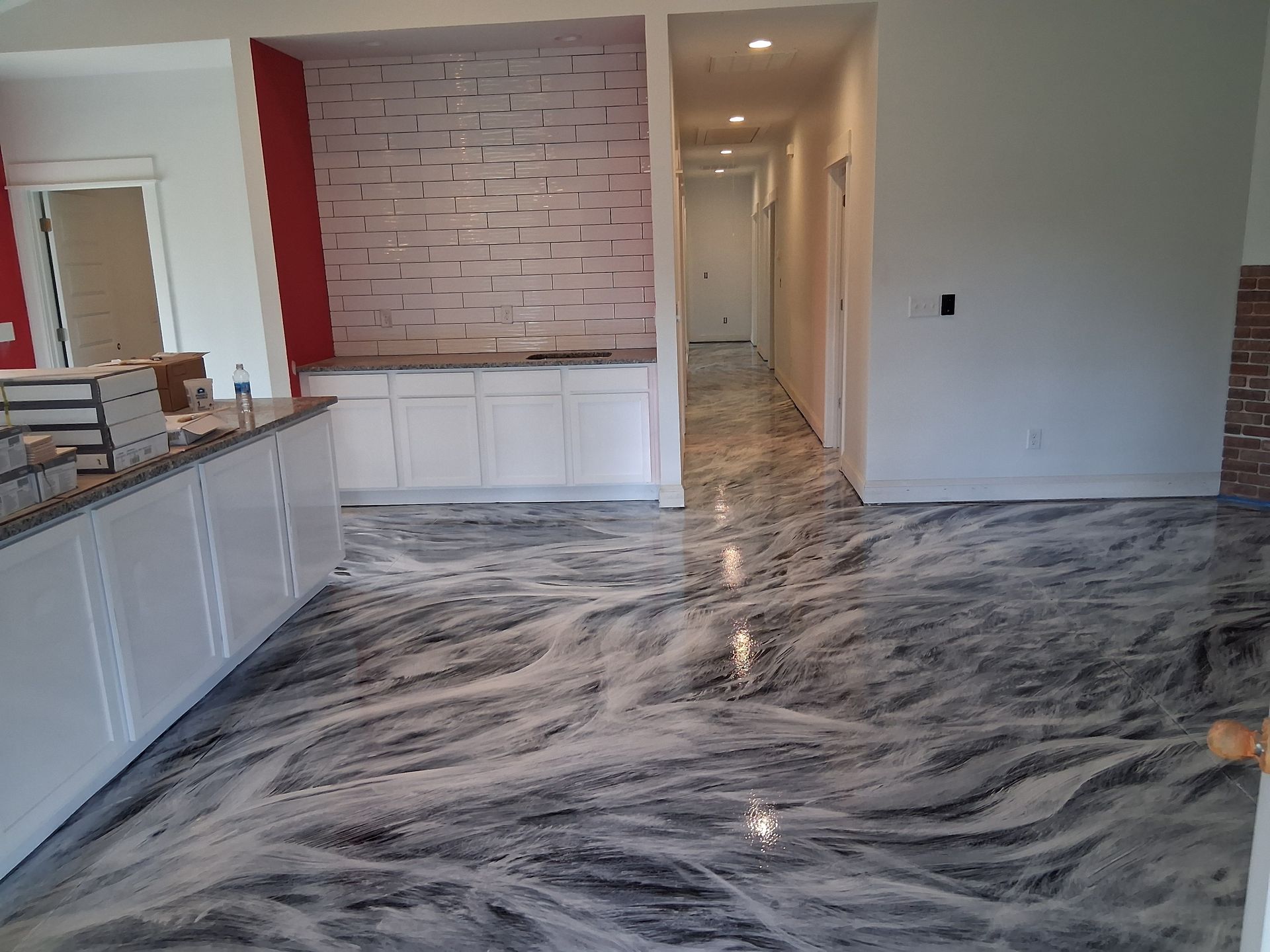 Modern room with glossy, grey-and-white marble-patterned epoxy flooring, white cabinetry, and a brick accent wall.