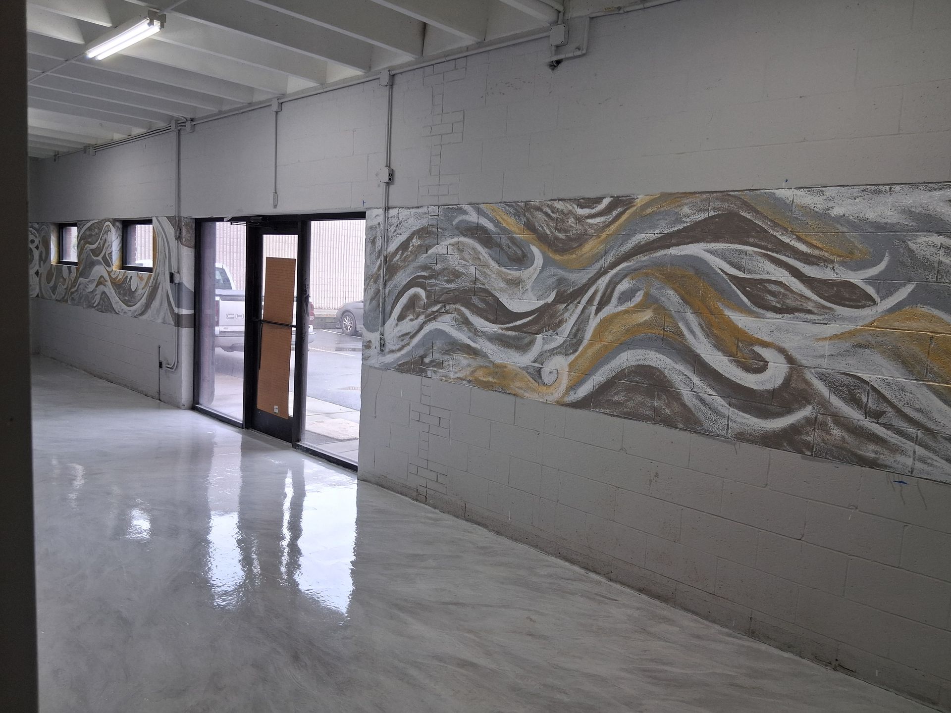A hallway with white glossy floors and a long mural of abstract, flowing brown, gold, and white waves on the grey wall.