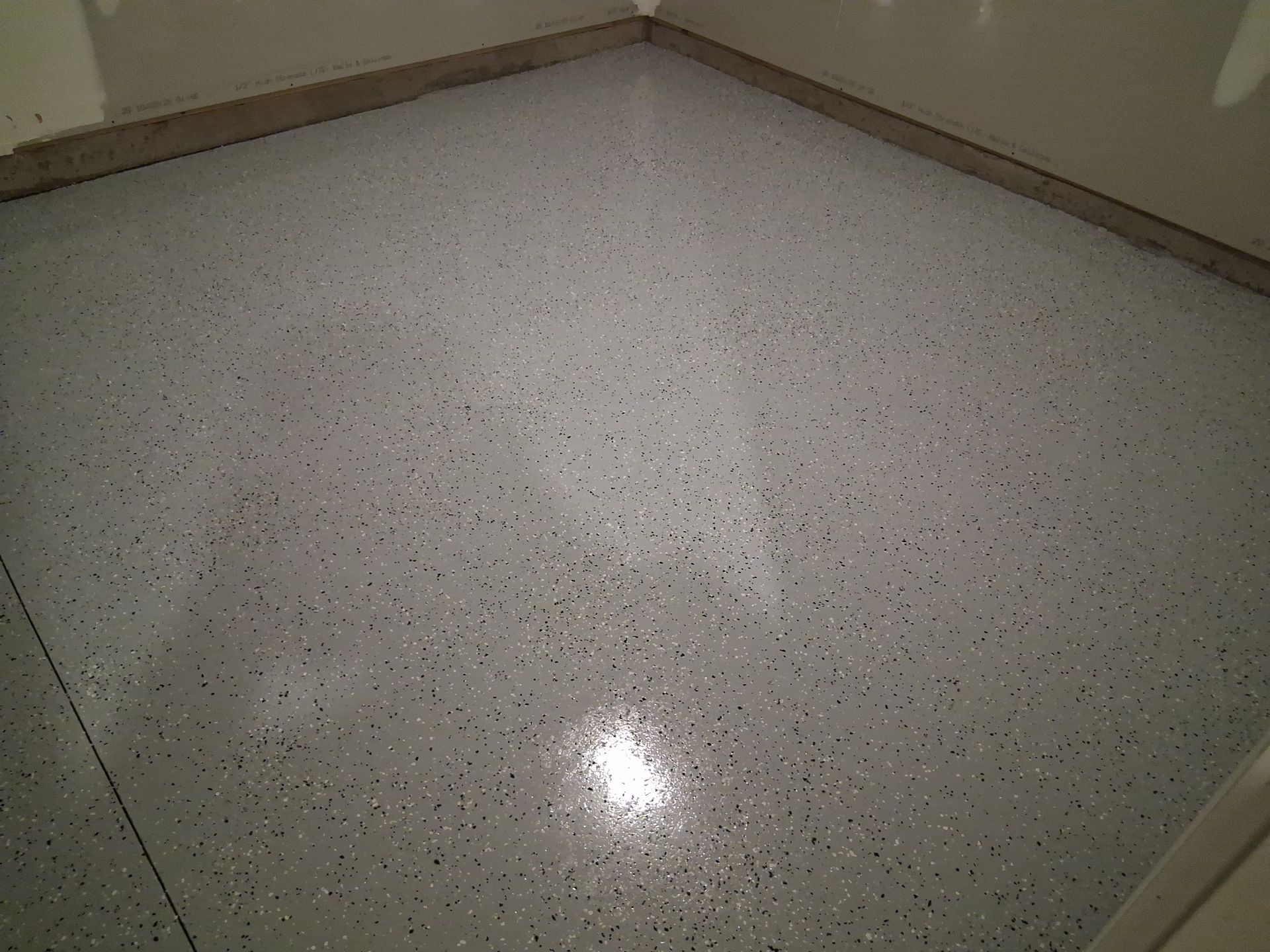 A smooth, glossy gray garage floor with black and white decorative paint flecks, surrounded by beige walls.
