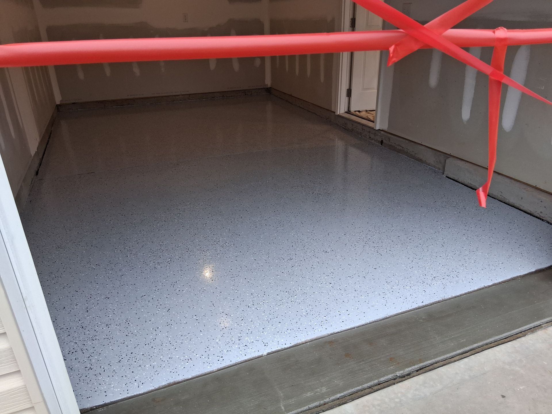 A newly finished garage floor with light gray epoxy coating and black speckles, blocked off by red caution tape.