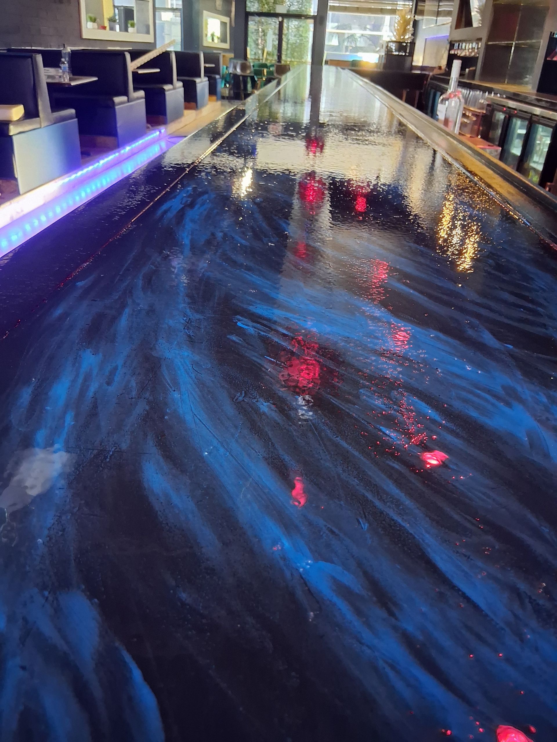A long bar top with a swirling blue and black epoxy finish, lit by glowing red points and a neon blue strip light.