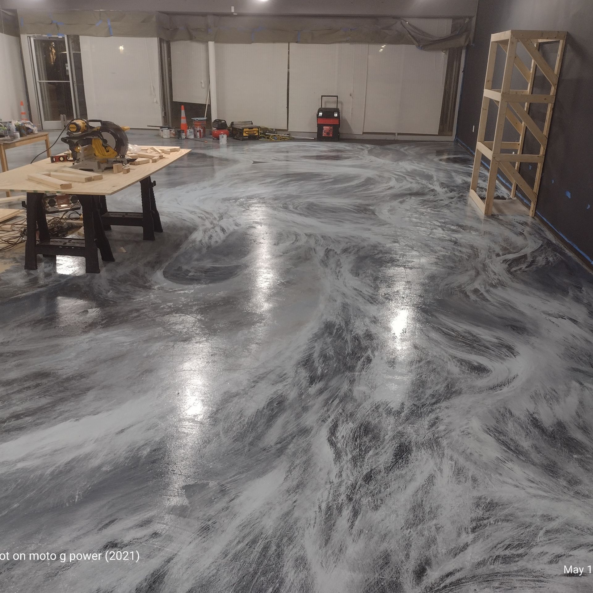 A workspace with a glossy, marbled gray and white epoxy floor, a miter saw on a workbench, and a wooden frame in the corner.
