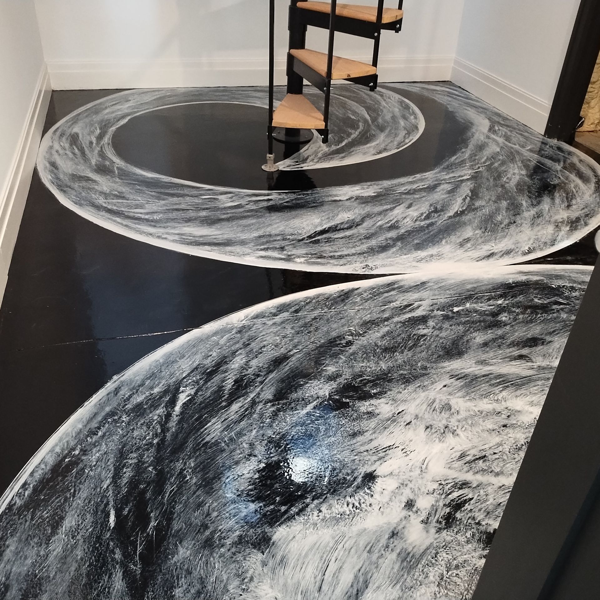 Black floor with a white, swirling paint design around a spiral staircase.