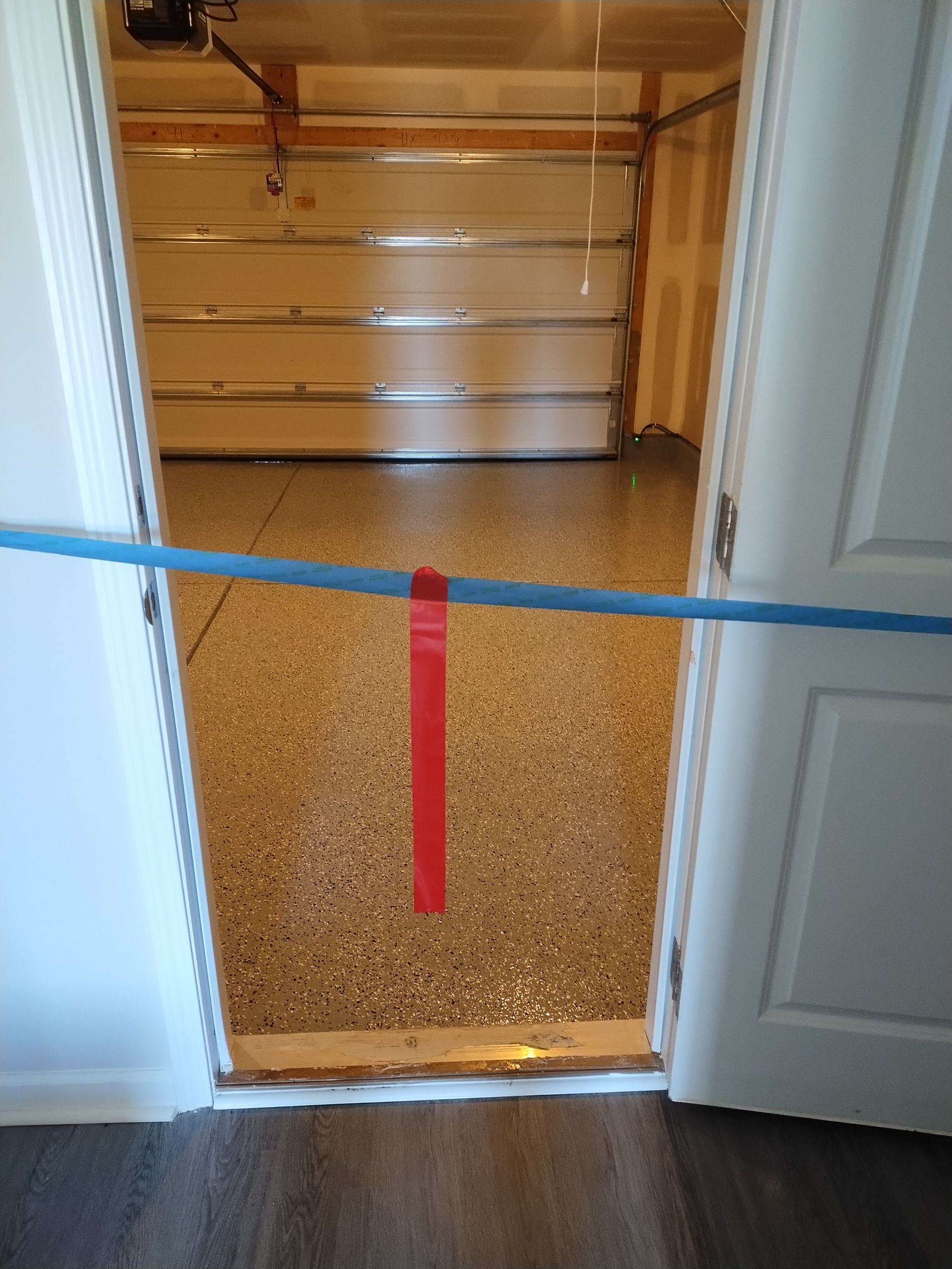 A doorway blocked by a blue tension pole with a hanging red strap, revealing a garage with a speckled floor.