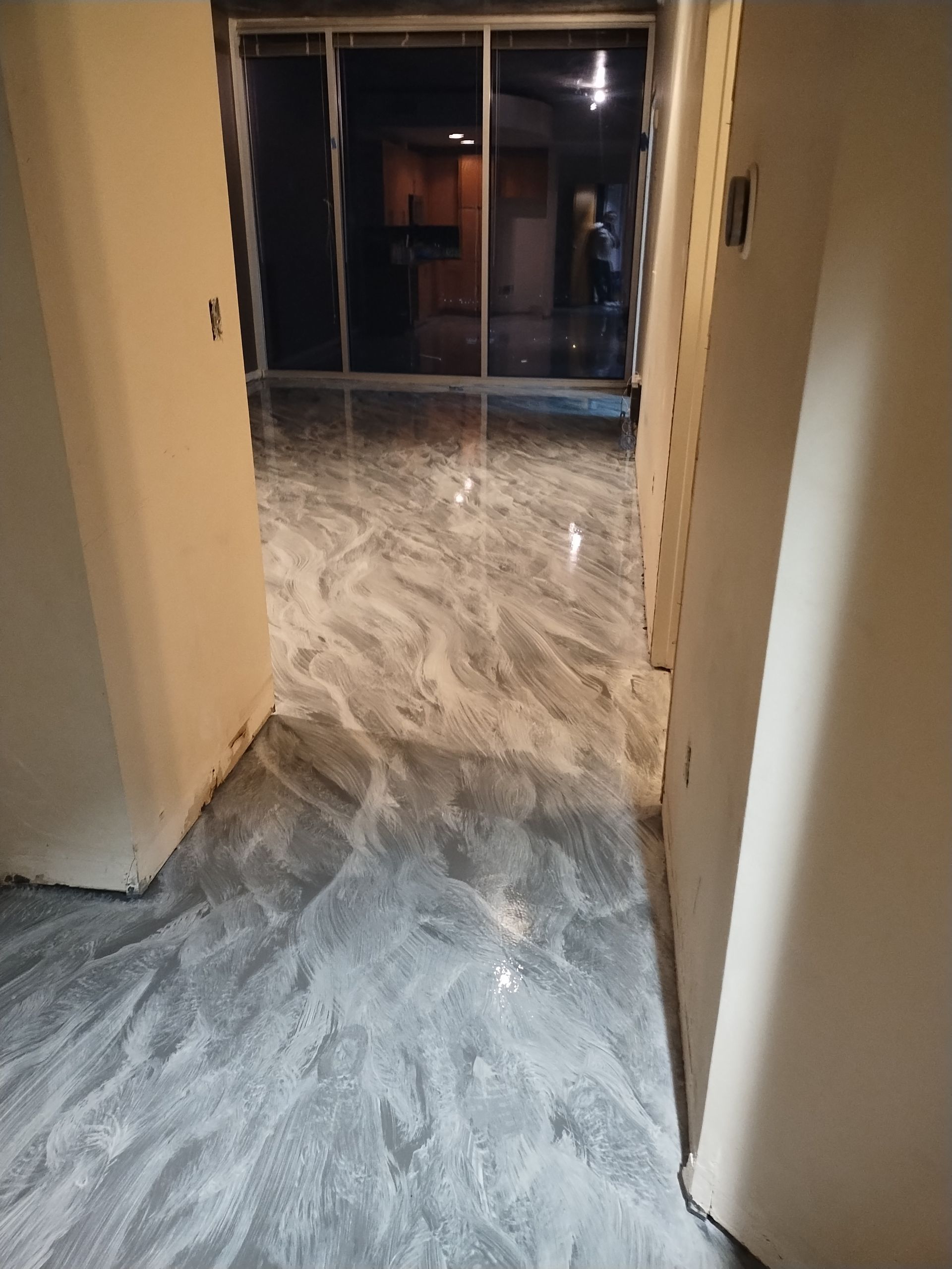 A hallway floor with a polished, marbled gray and white epoxy finish, leading toward a glass sliding door.