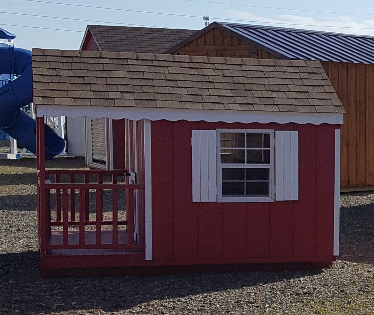 A red playhouse with white shutters and a blue slide in the background