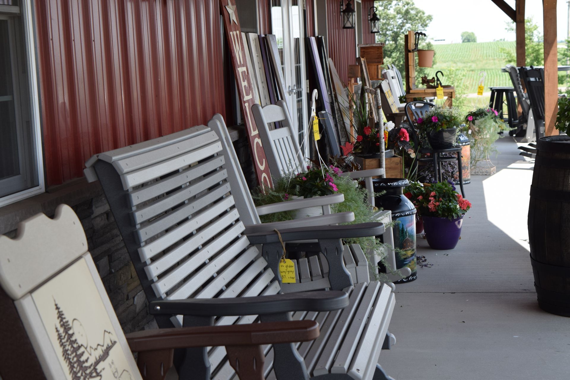 A row of chairs are sitting on a porch in front of a red building.