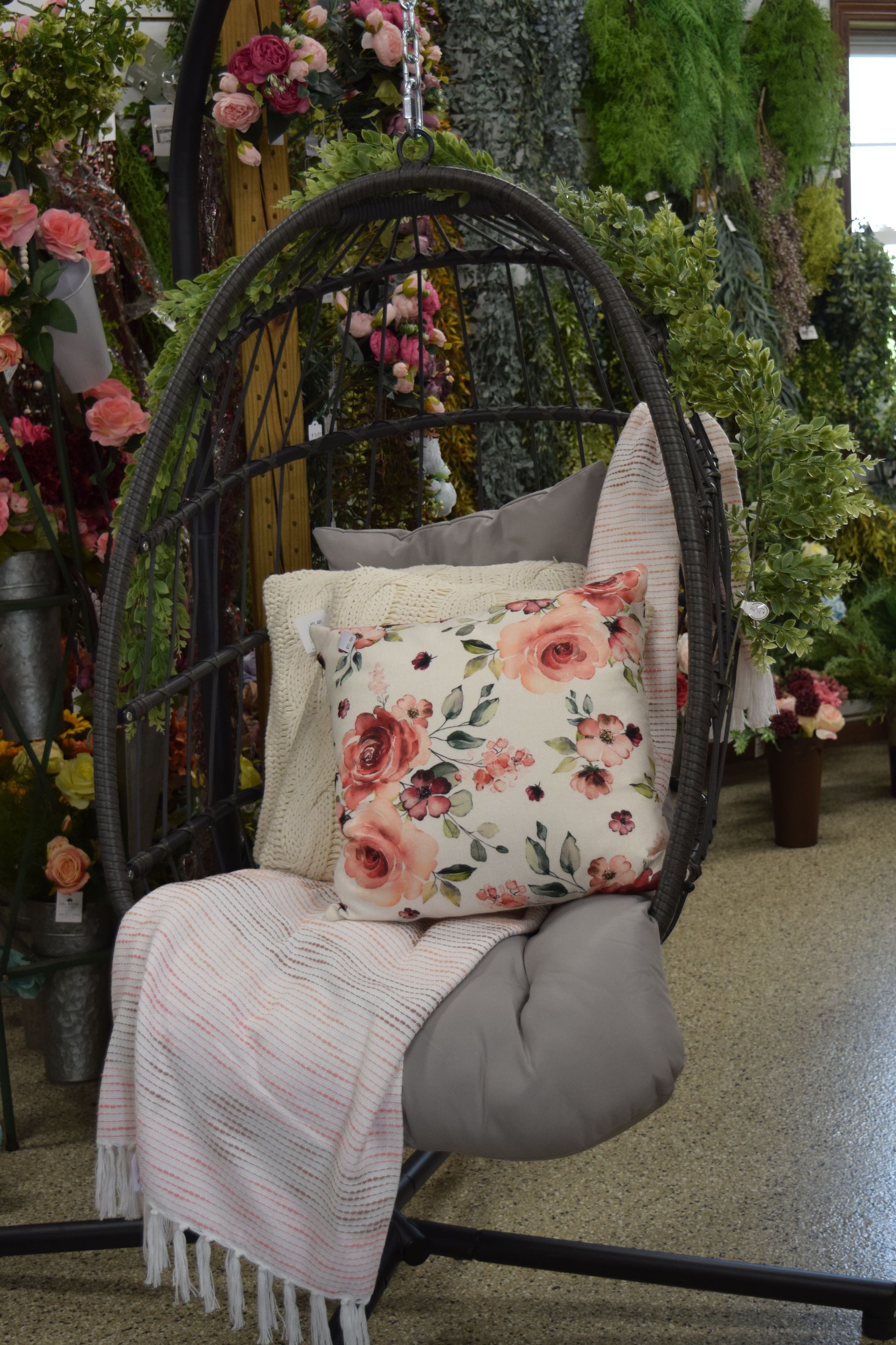 A hanging chair with a floral pillow and a blanket on it.
