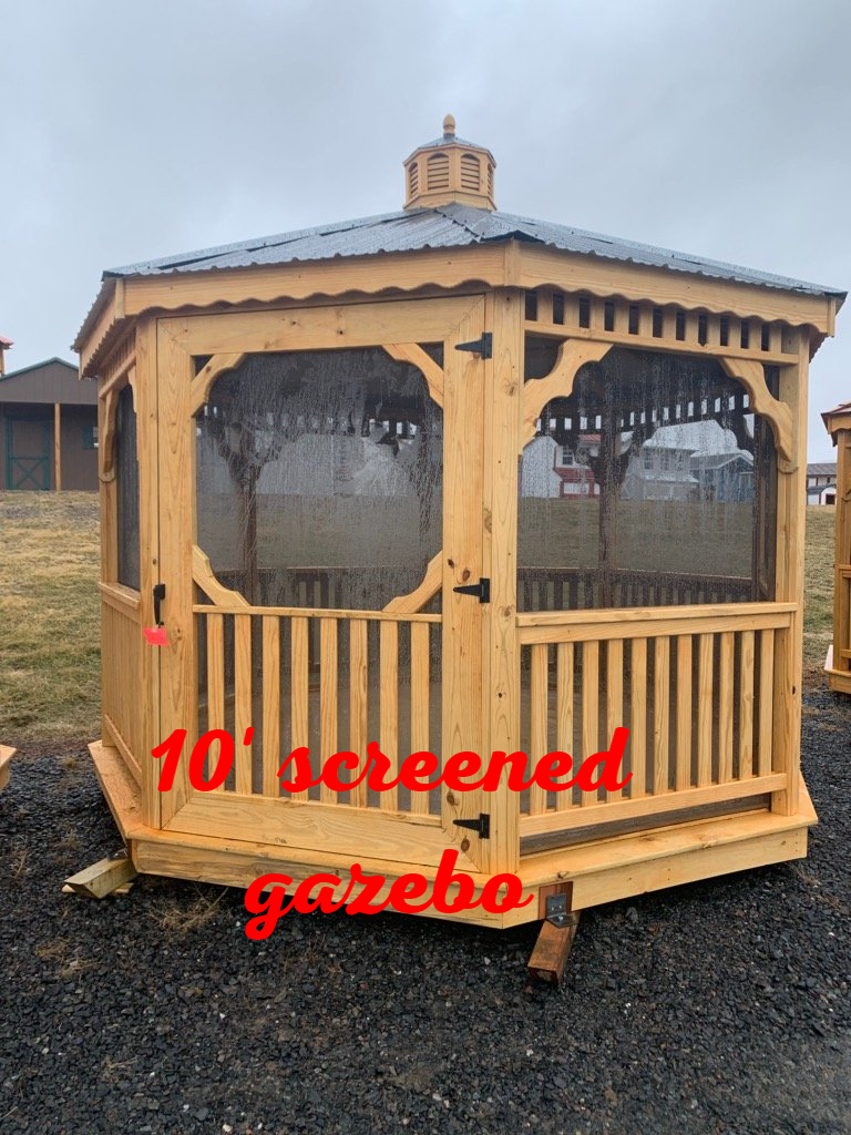 A wooden gazebo with a screened in porch is sitting in the dirt.