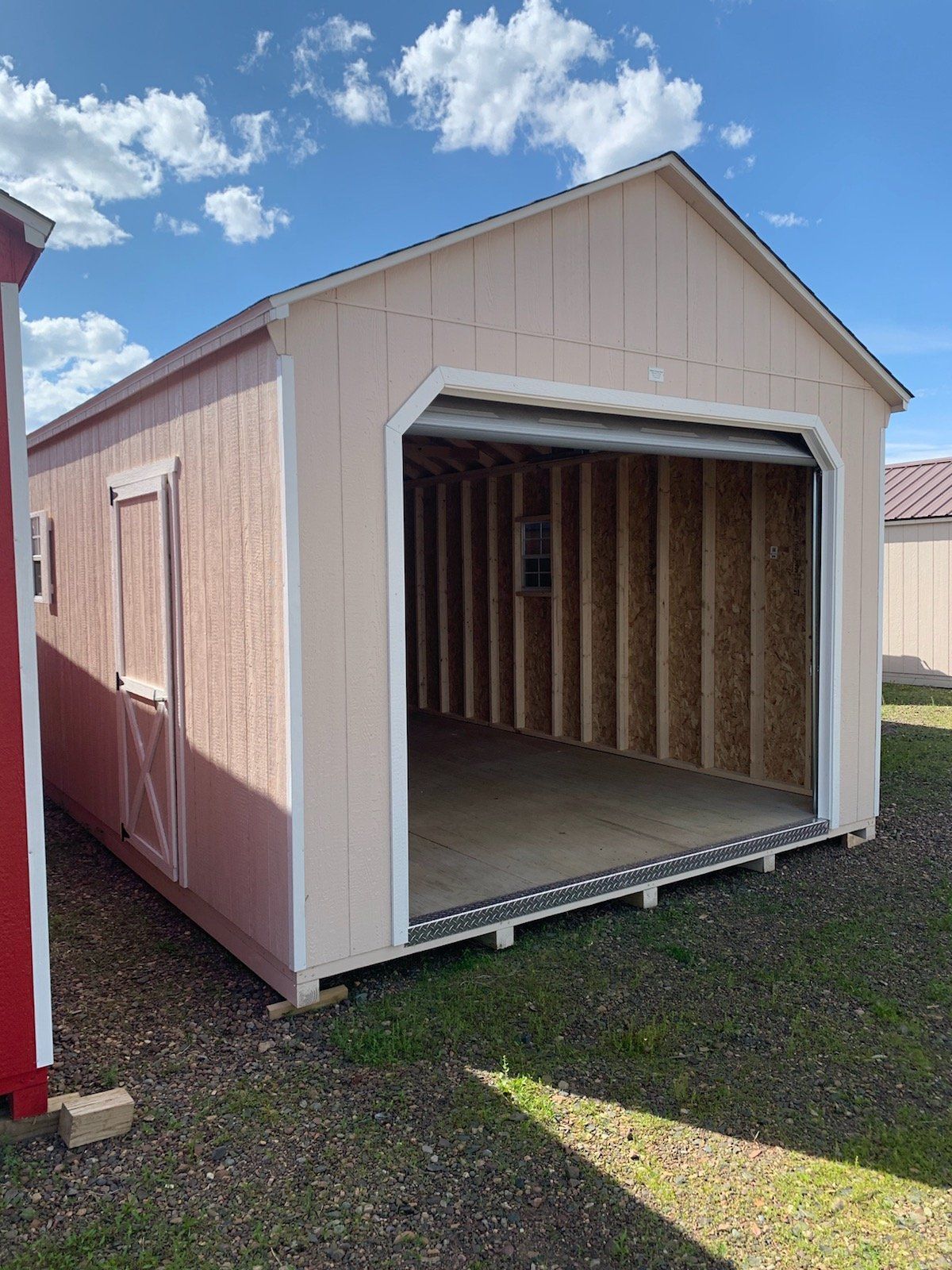 A shed with a garage door open is sitting on top of a lush green field.
