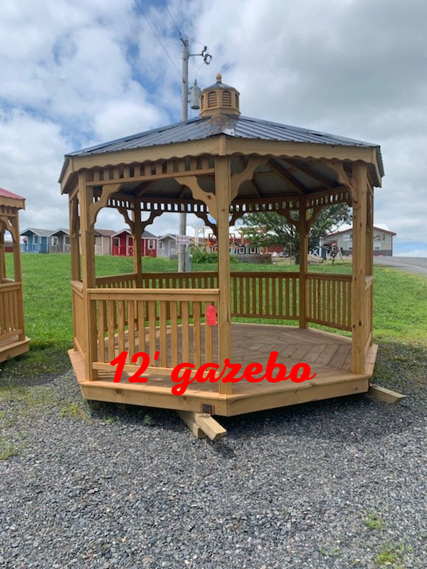 A wooden gazebo is sitting on top of a gravel lot.