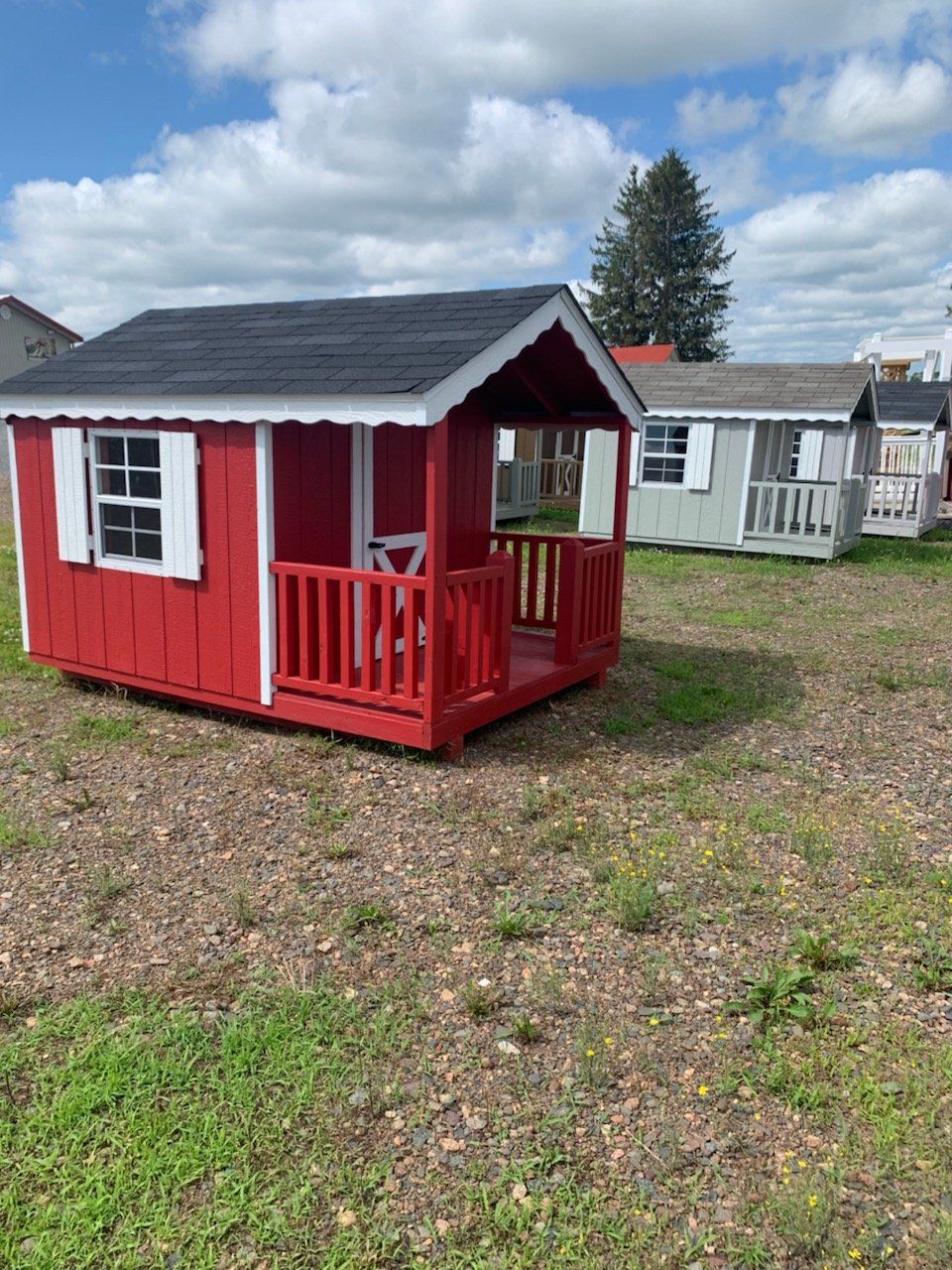 A red and white playhouse with a porch in a field.
