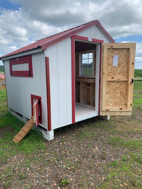 A white and red chicken coop with the door open in a field.