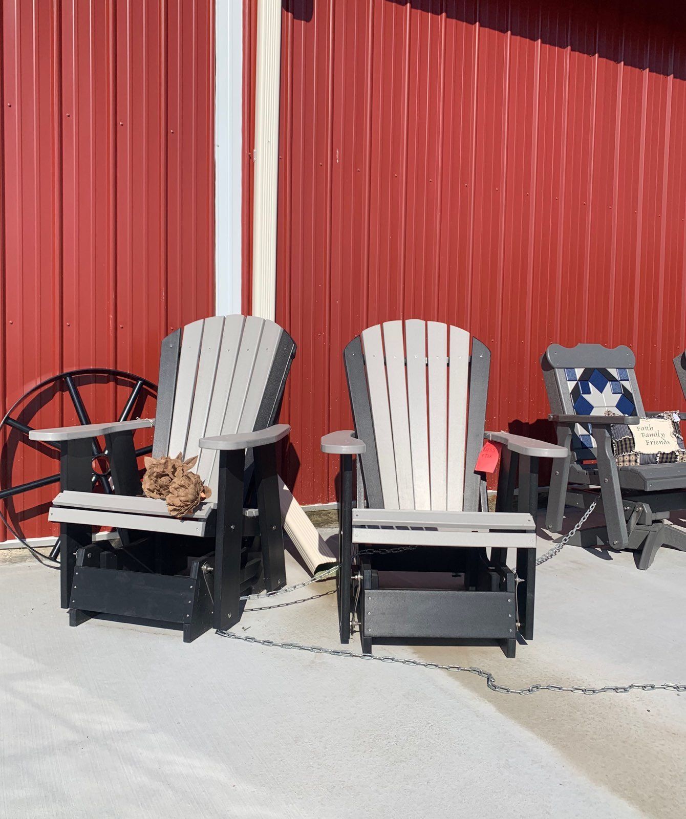 Two adirondack chairs are sitting in front of a red barn.