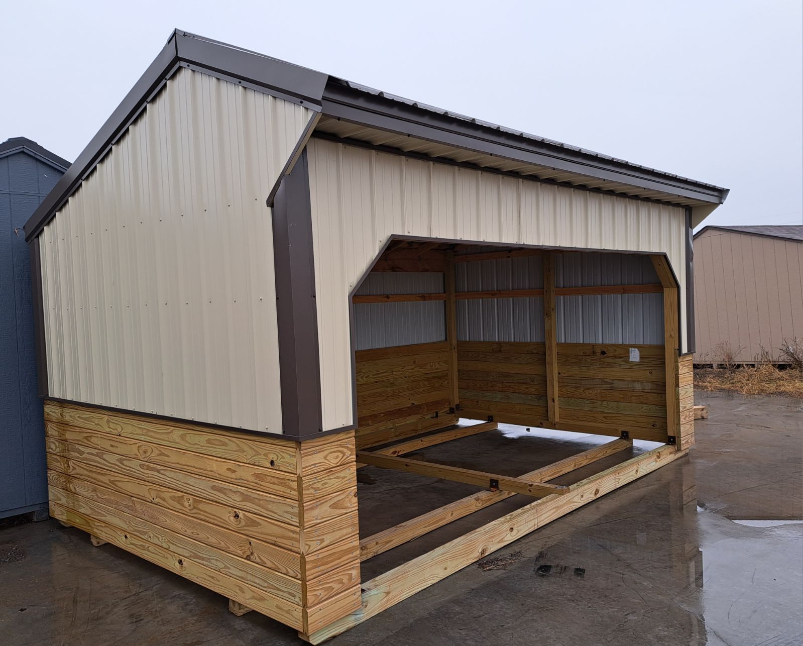 A wooden shed with a metal roof is sitting in a parking lot.