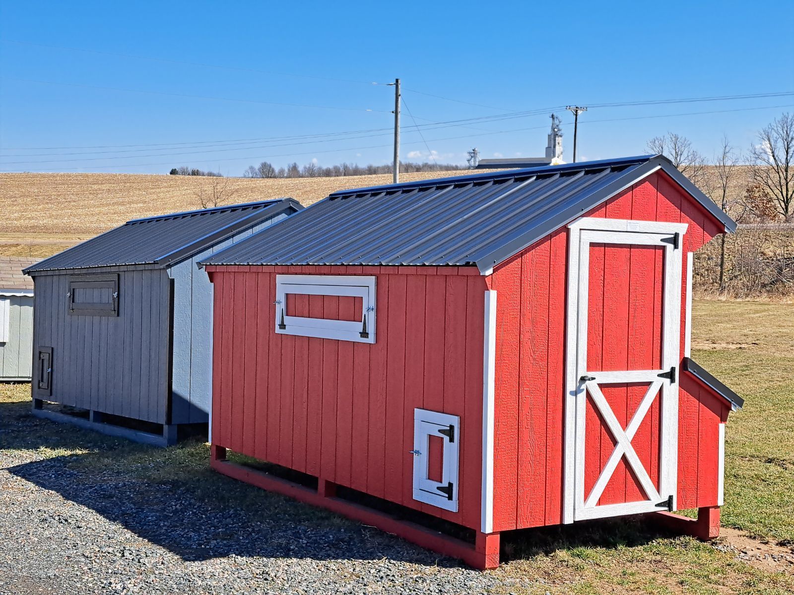 A red chicken coop is sitting next to a white chicken coop in a field.