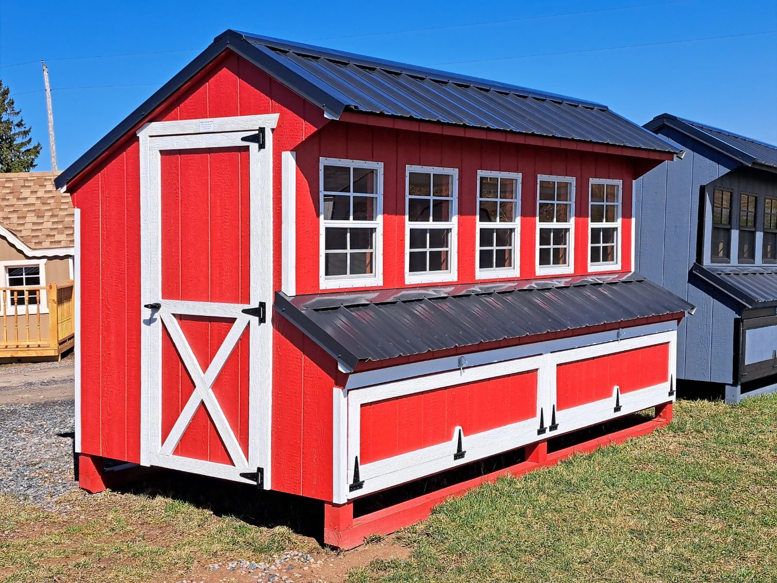 A red and white chicken coop with a black roof is sitting on top of a lush green field.