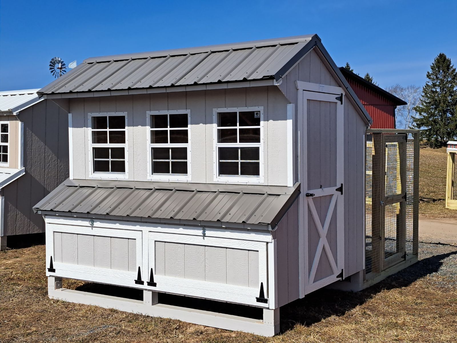 A chicken coop with a gray roof and white trim is sitting in the grass.