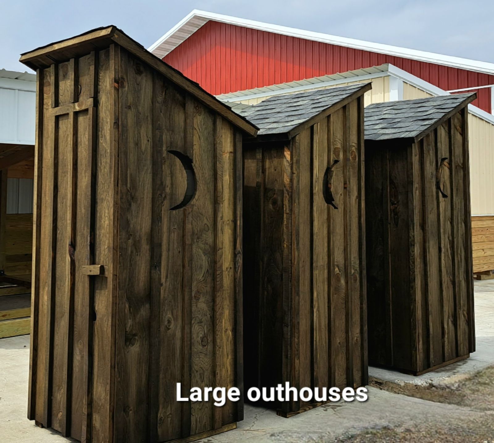 Three large outhouses are lined up in front of a red barn