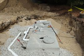 Septic tank installation in a gravel-lined pit with white pipes, tools, and dirt.