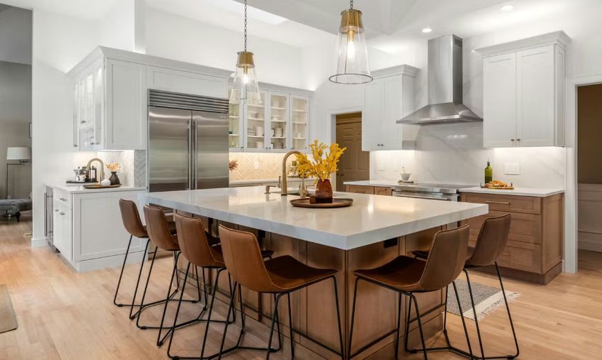 Modern kitchen with large island and brown leather bar stools. White and wood cabinets.