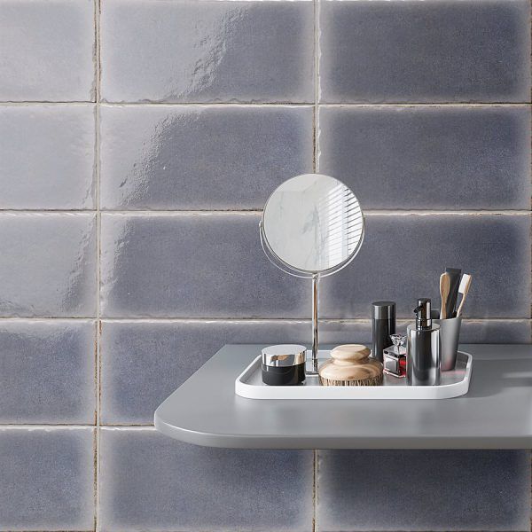 A vanity with blue tiles, a mirror, and makeup on a shelf.
