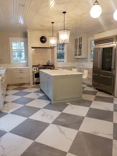 Spacious kitchen with checkered floor, island, and stainless steel refrigerator. Light fixtures hang from the ceiling.