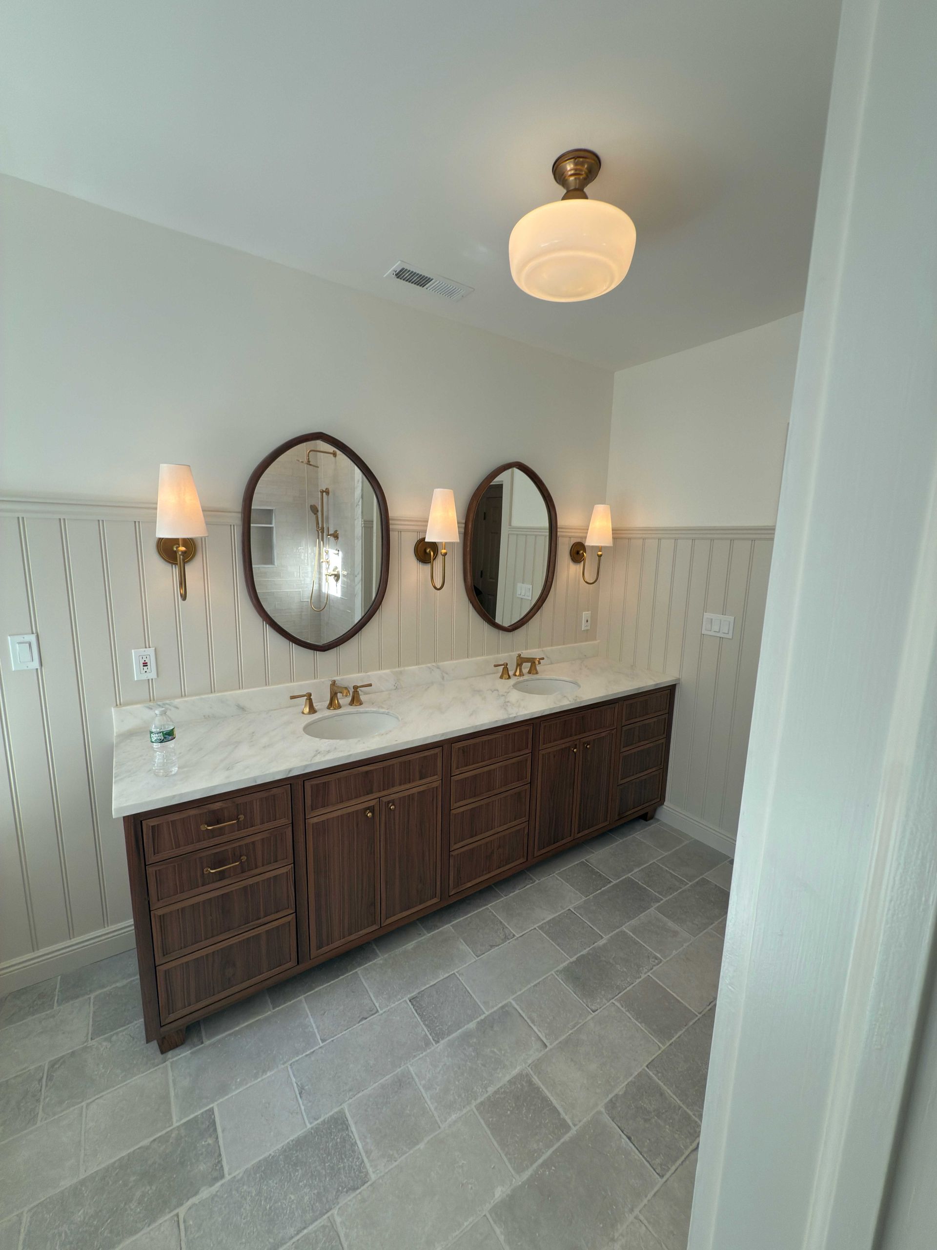 Bathroom with a long dark wood vanity, oval mirrors, and sconce lighting.