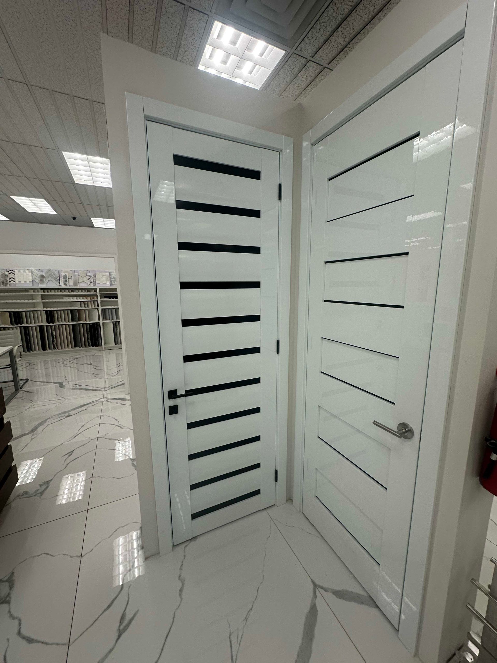 Two white doors with horizontal black inlays, in a showroom.