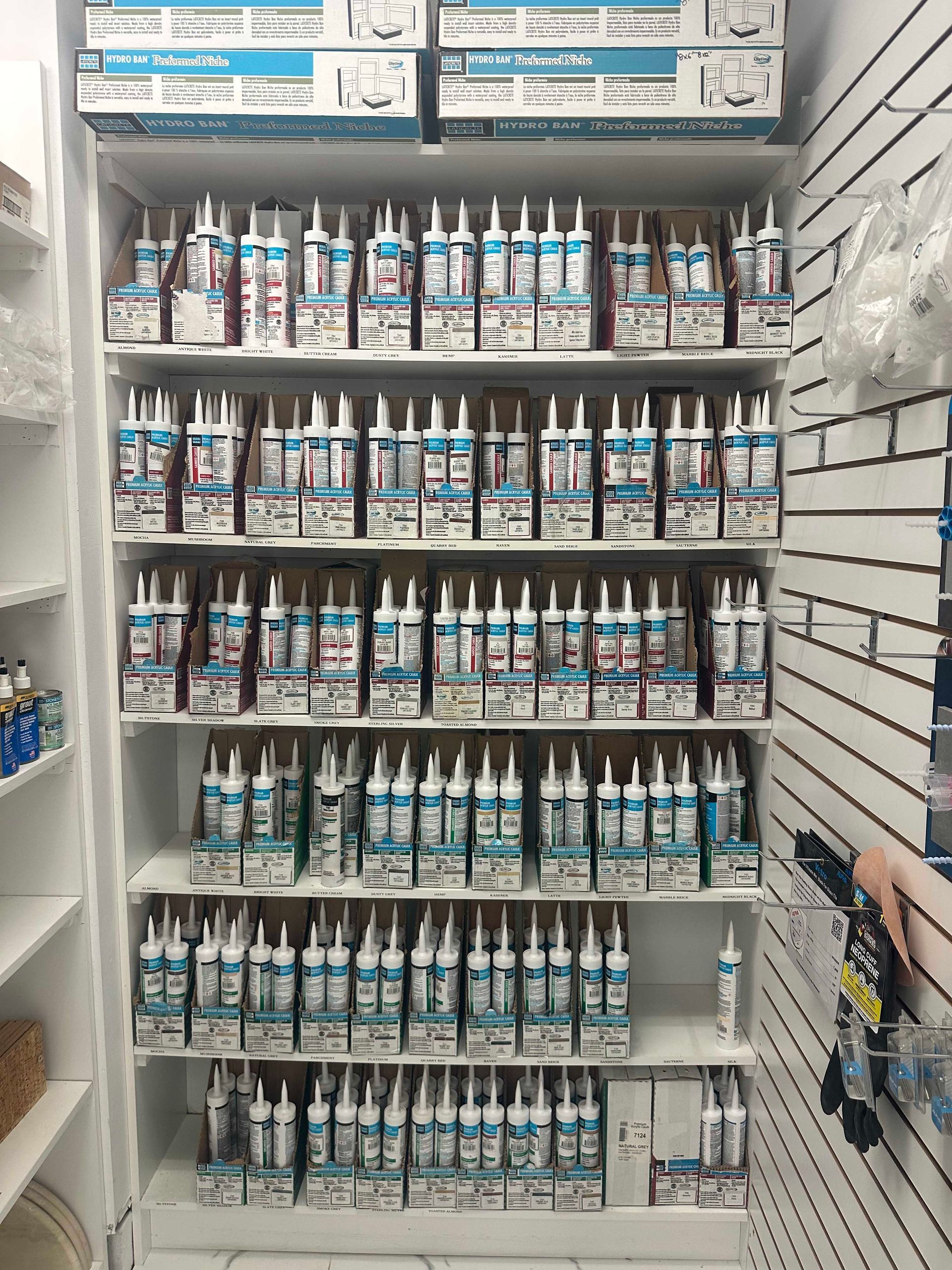Shelves stocked with tubes of sealant in a hardware store setting. White and blue packaging is visible.