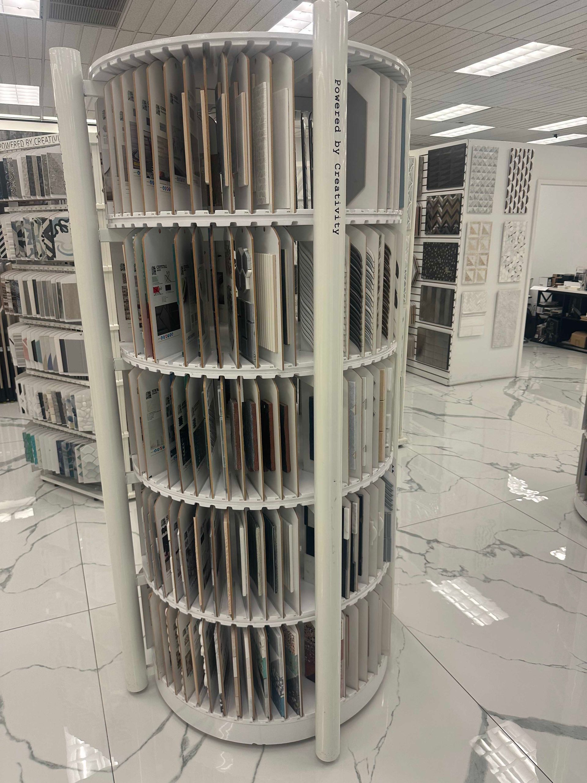 A cylindrical display rack with tile samples in a store. White structure with many tile displays.