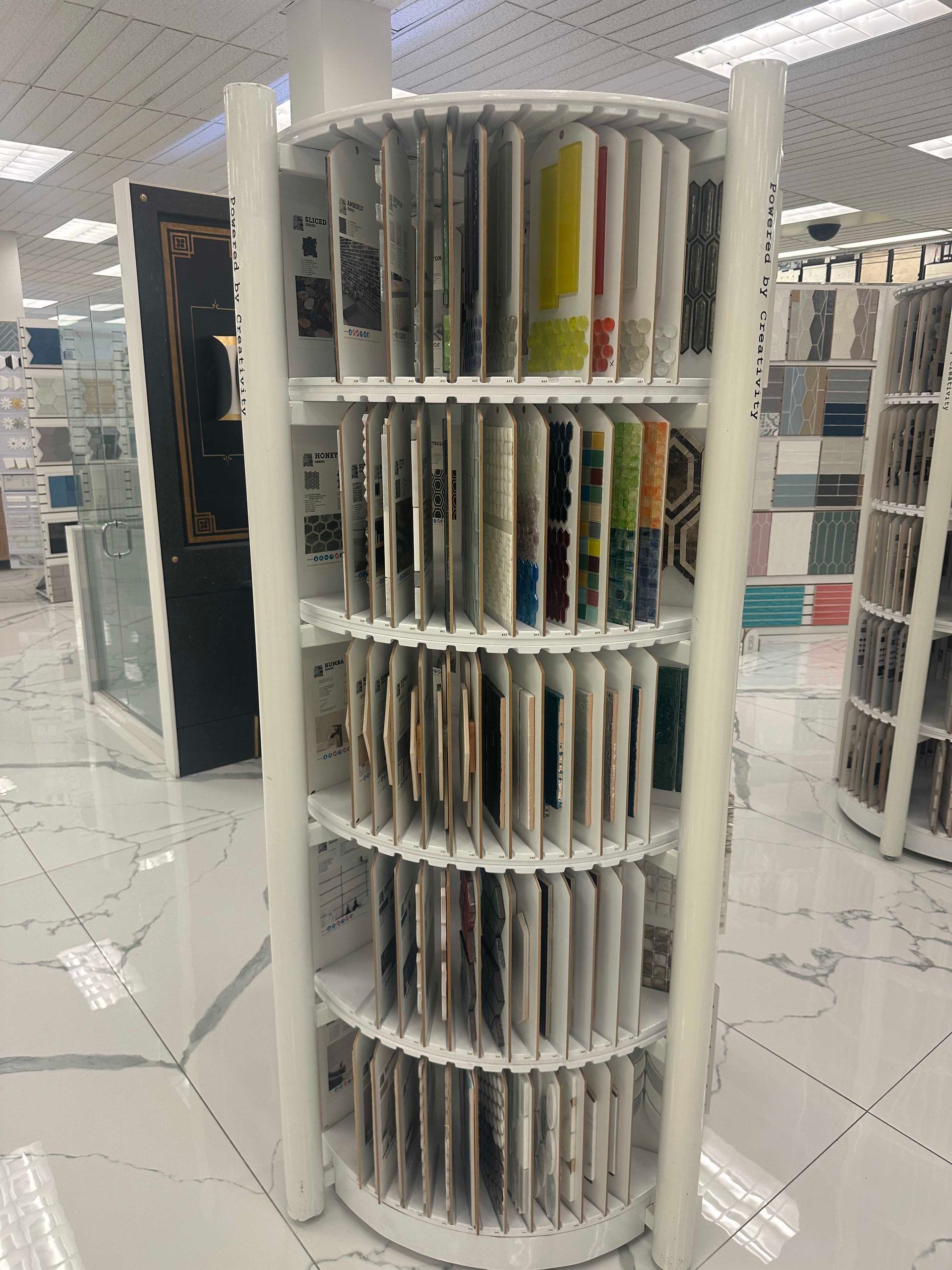 White rotating display rack holding numerous tile samples in a showroom.