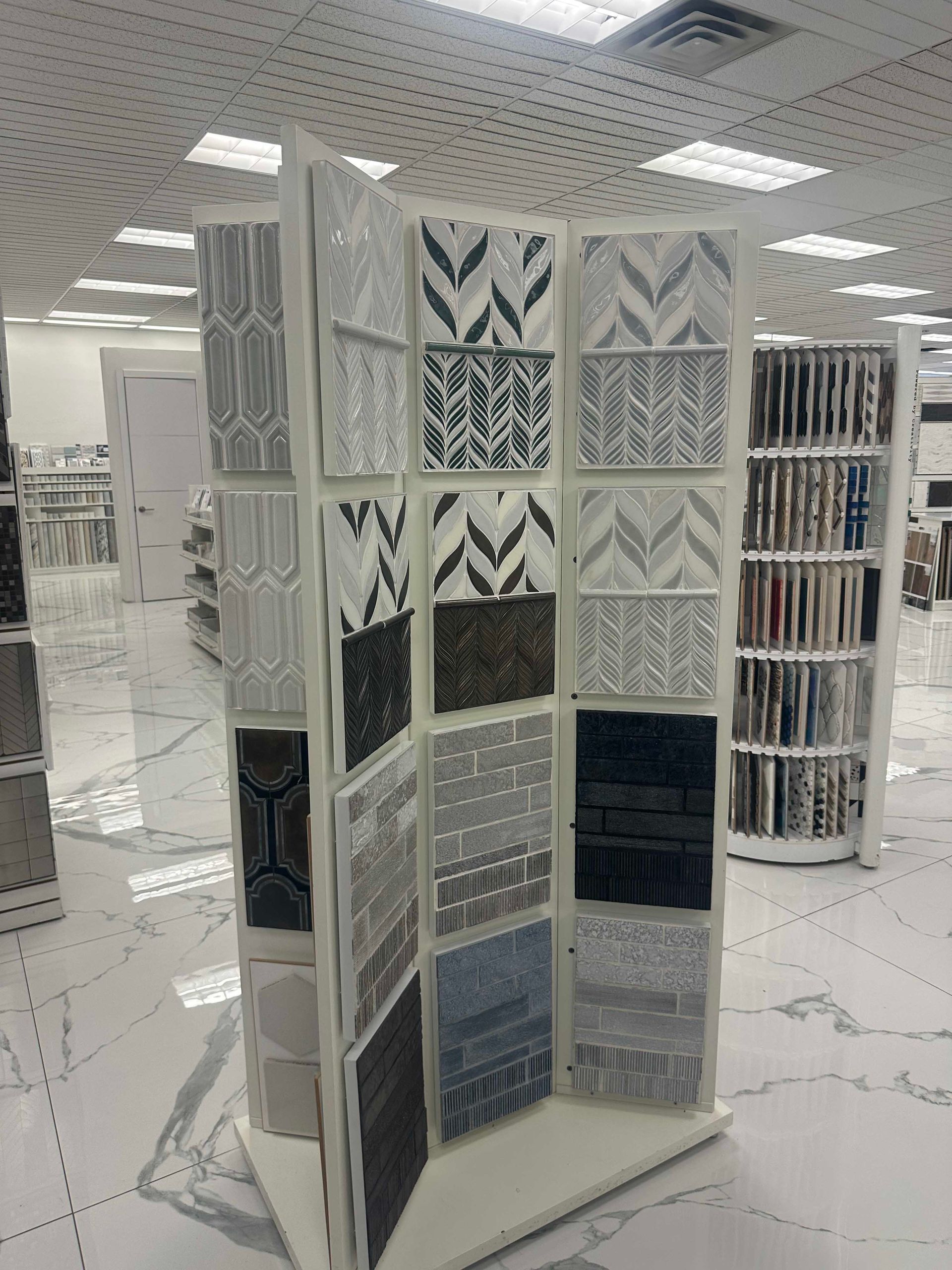Display of various patterned tiles in a showroom. White shelves and flooring. Brightly lit room.