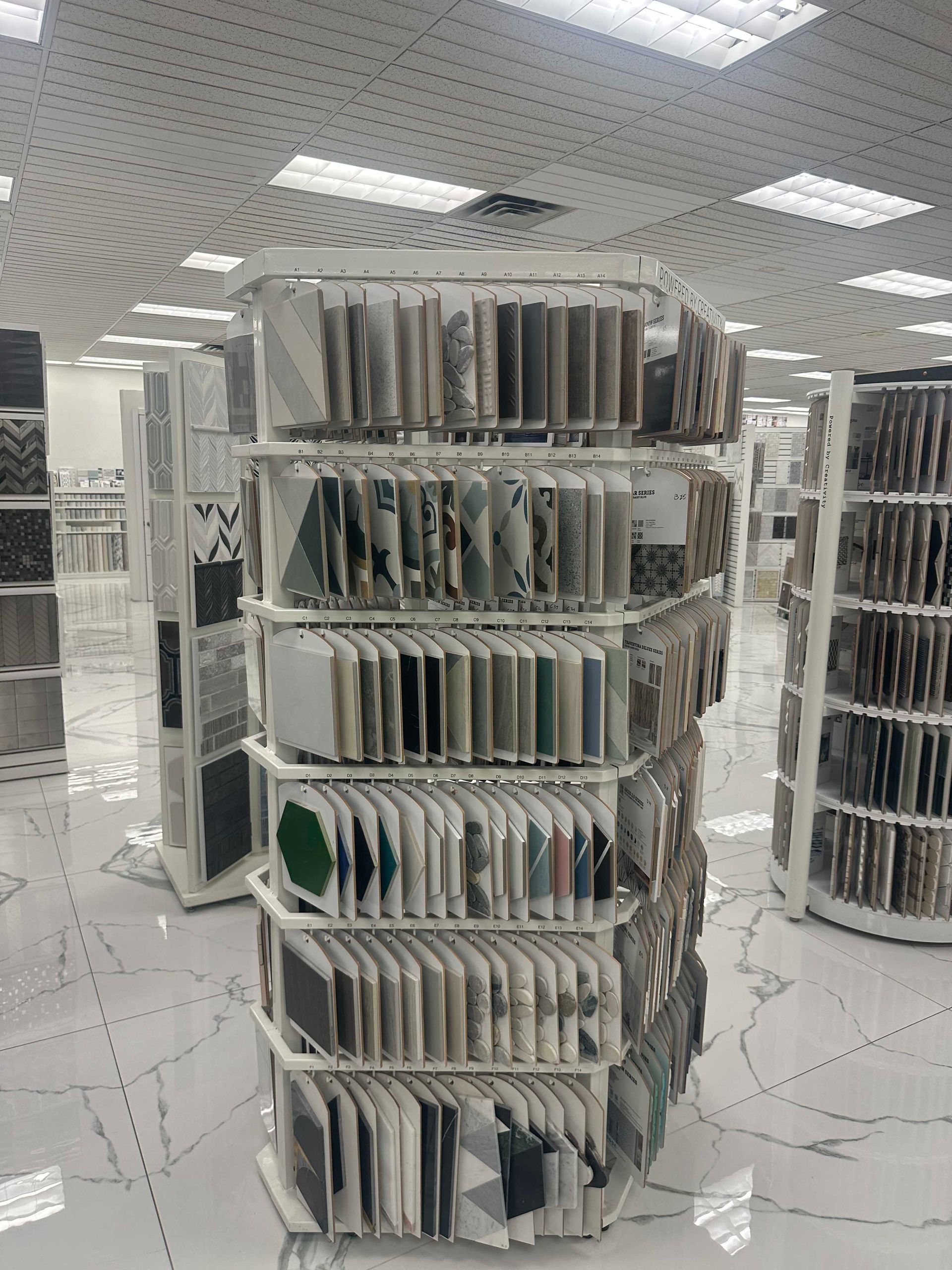 Shelves displaying tile samples in a brightly lit showroom. White shelving units with various tile designs.