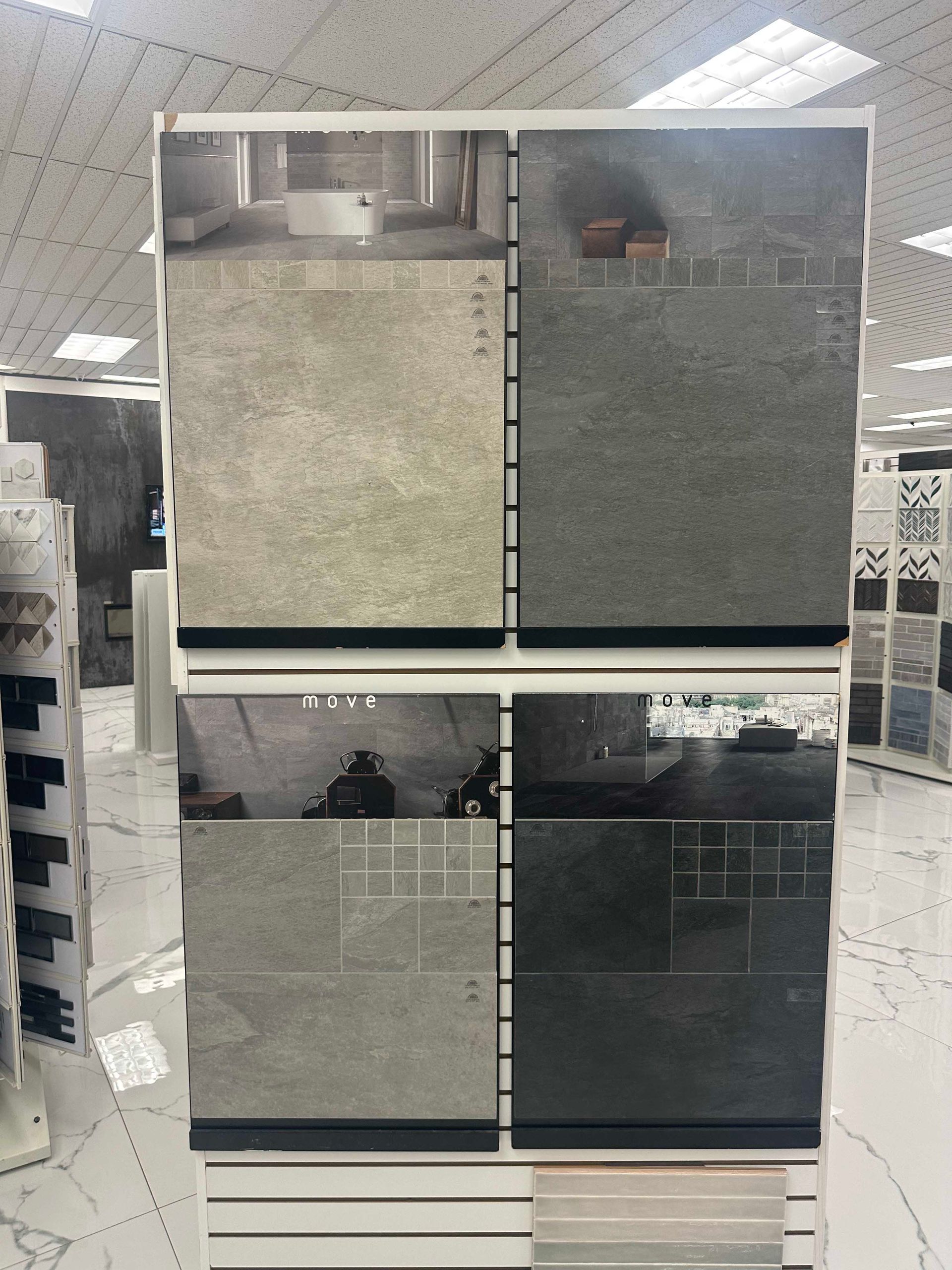 Display of four large, textured tile samples in shades of gray, arranged in two rows.