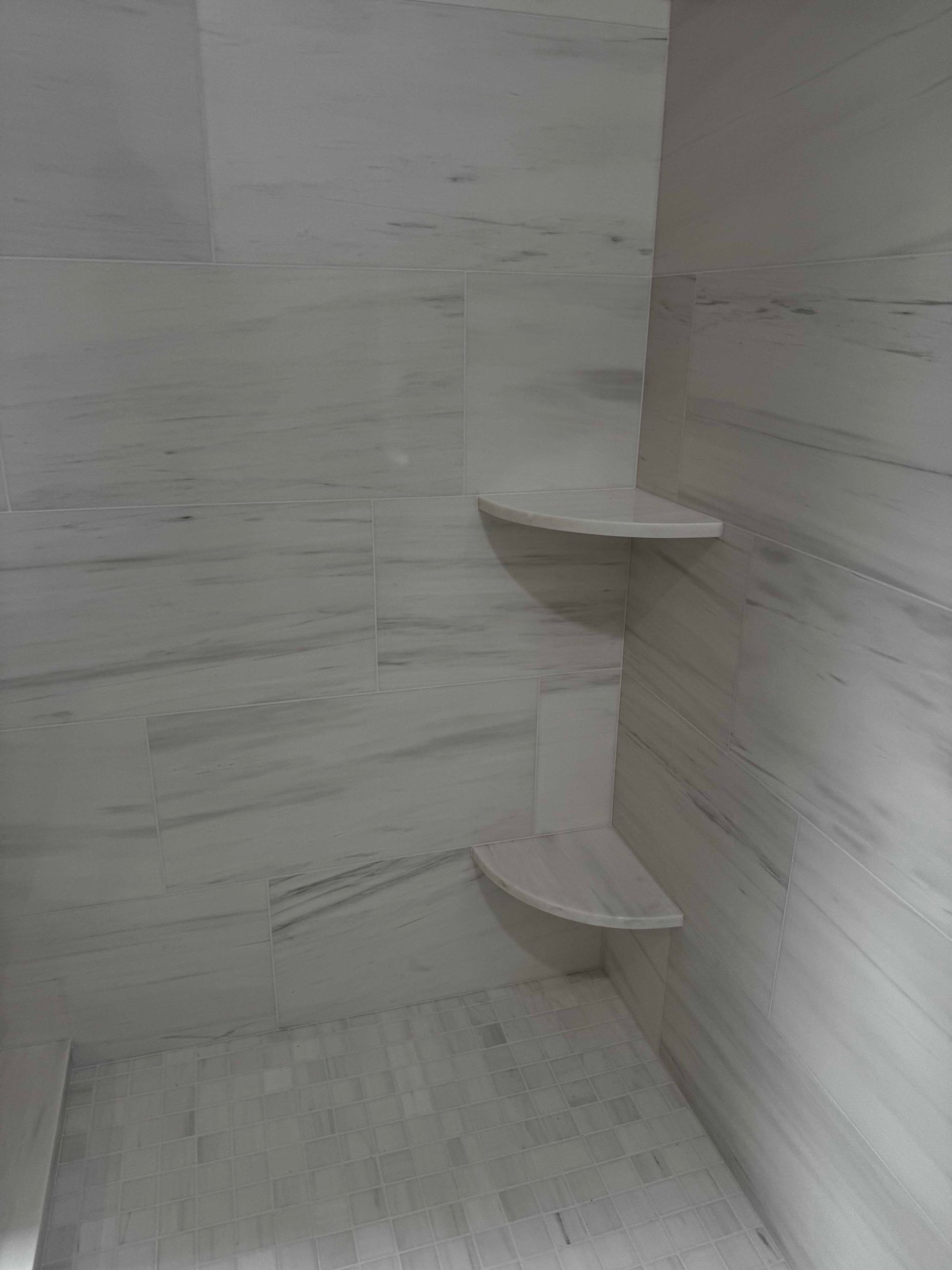White tiled shower with built-in shelves in corner.