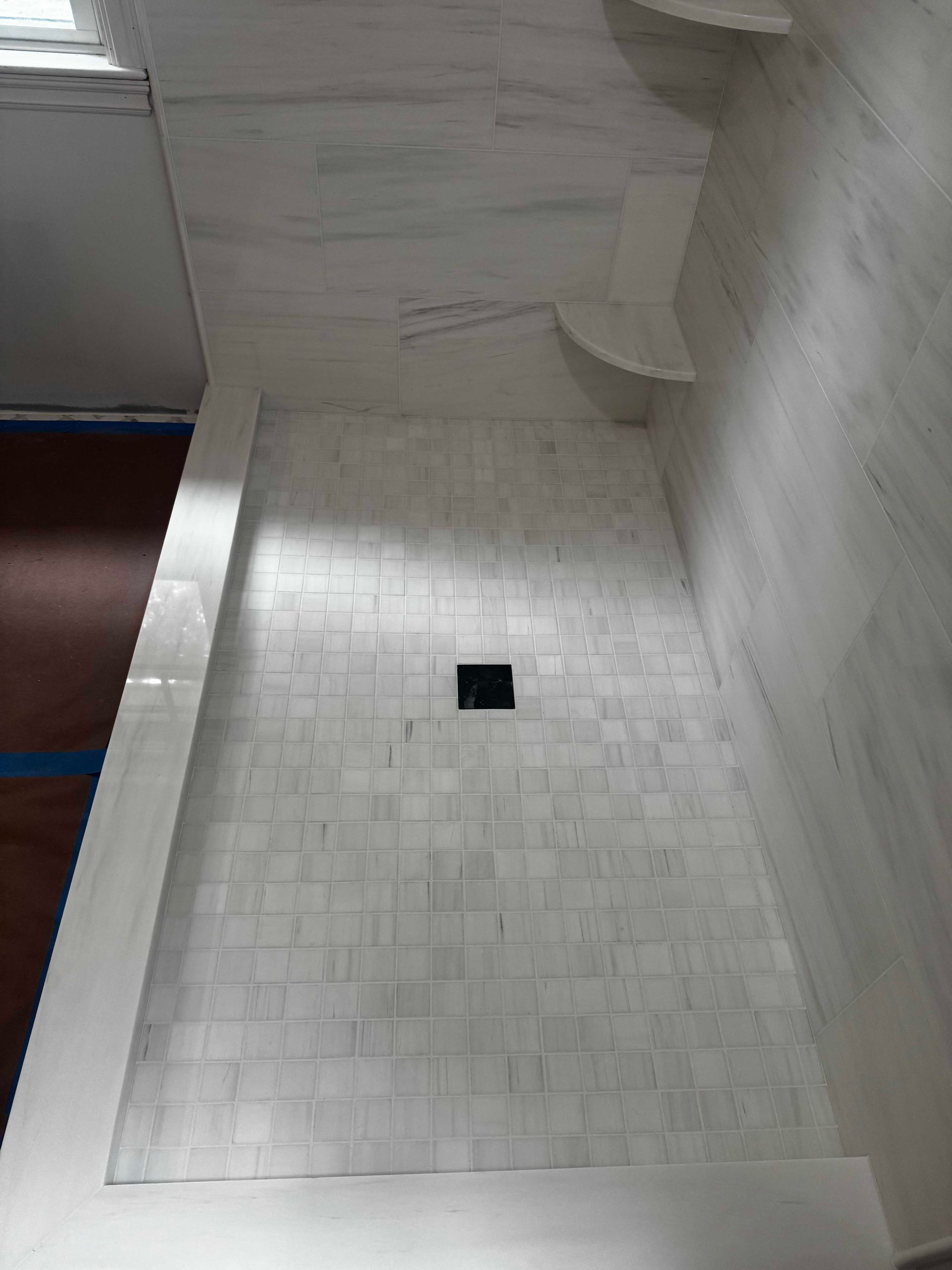 White tiled shower stall with corner shelves and a central drain.