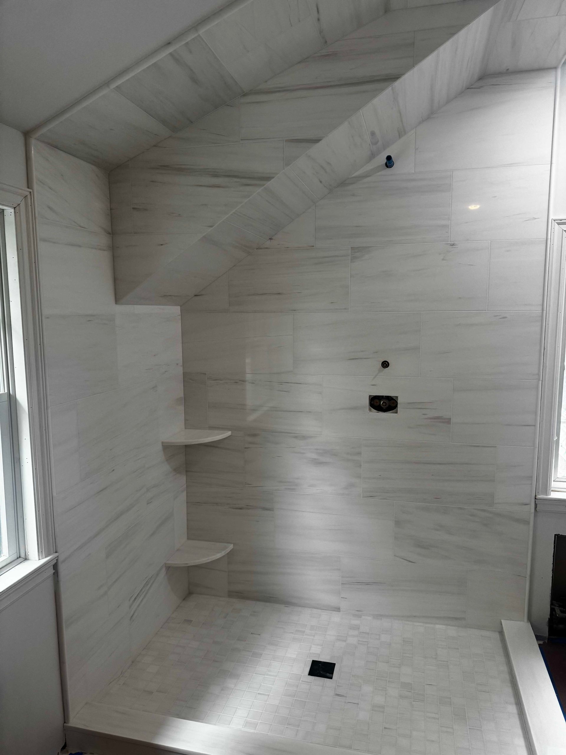 White tiled shower with built-in shelves, angled ceiling, and window frames.