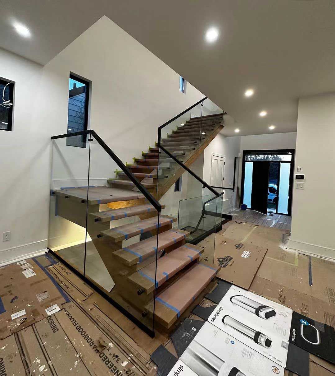Modern staircase with wooden steps, glass railings, and black handrails in a newly constructed home.