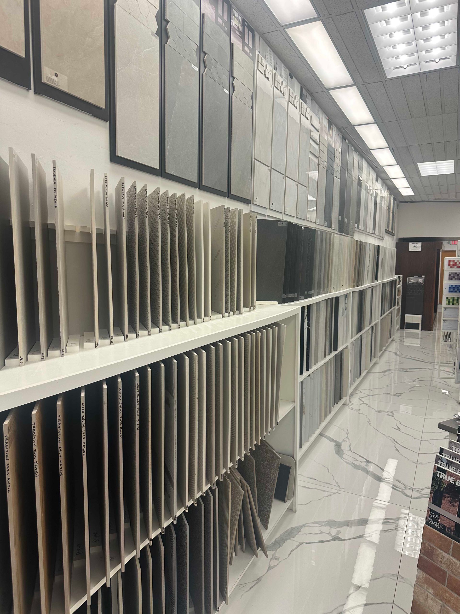 Tile showroom with rows of displayed tiles on shelves and walls.
