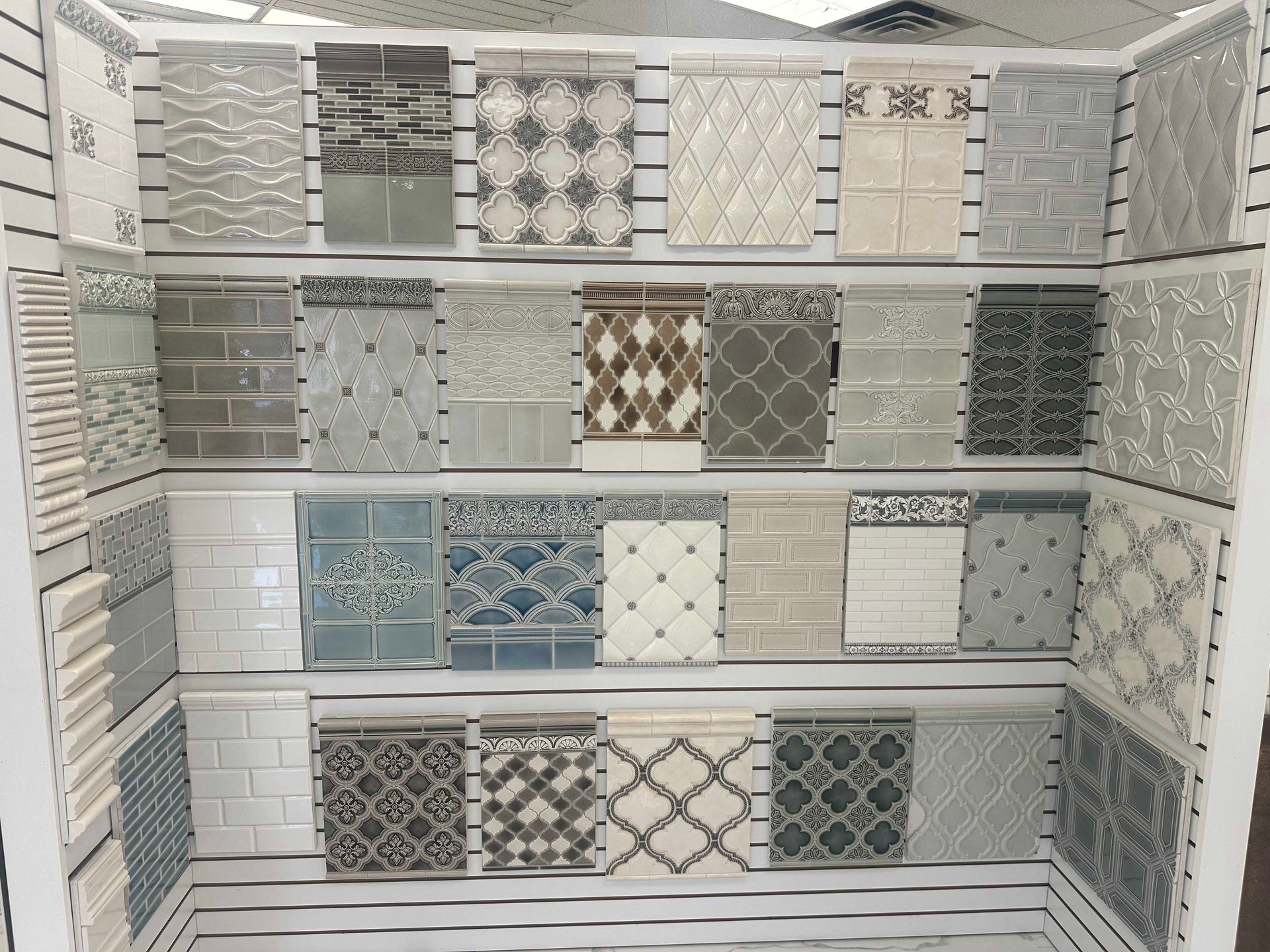 Display of various decorative tiles in neutral colors on shelves.