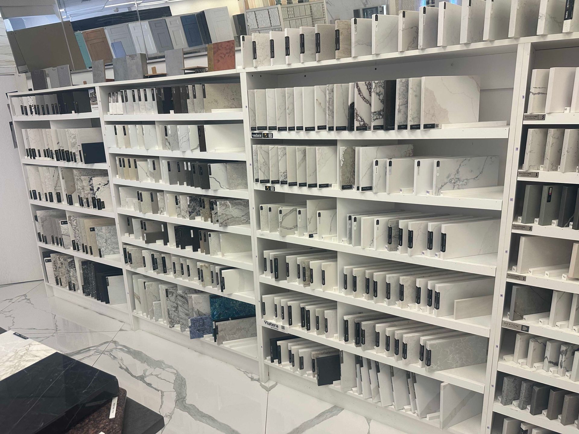 Shelves filled with various stone samples in a showroom; mostly white and gray, organized vertically.