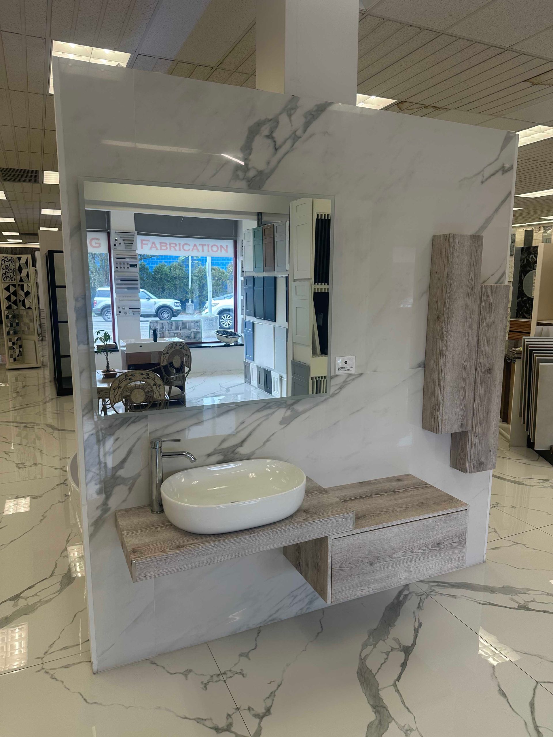 Bathroom display with a marble-patterned wall, sink, mirror, and wooden shelf.