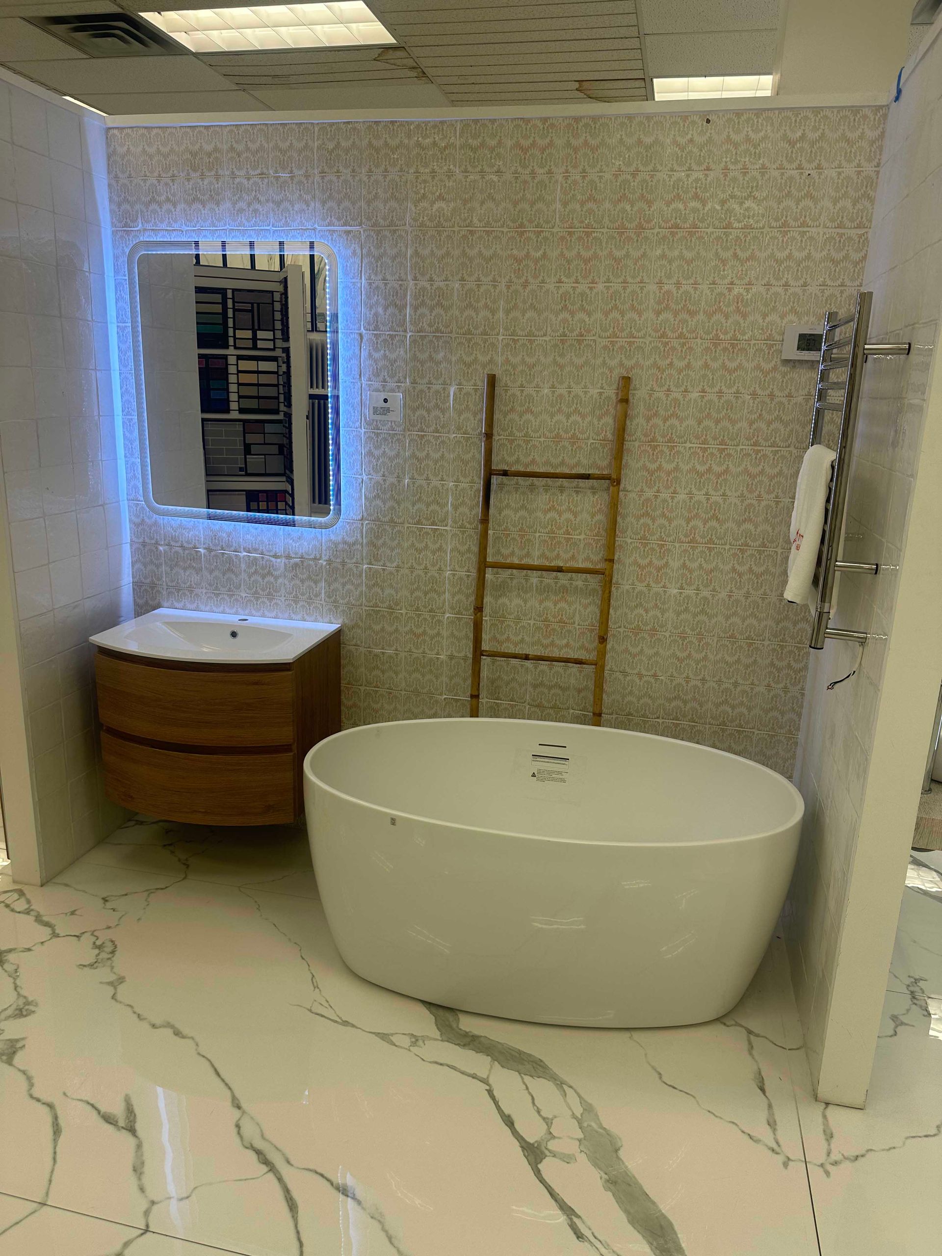 Bathroom with white tub, wooden vanity and ladder, lit mirror, and patterned tile.