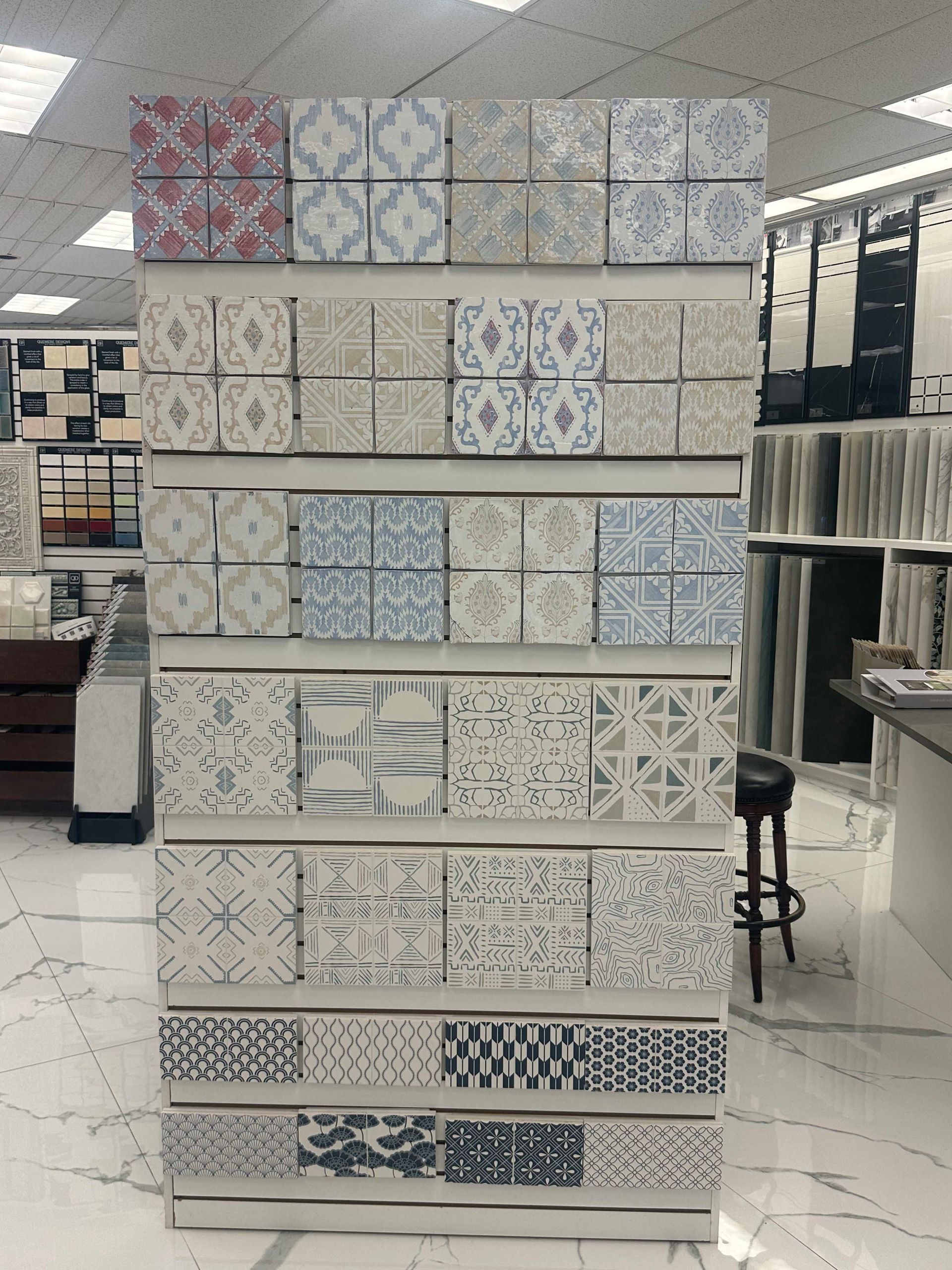 Tile display rack with various patterned square tiles in a showroom setting.