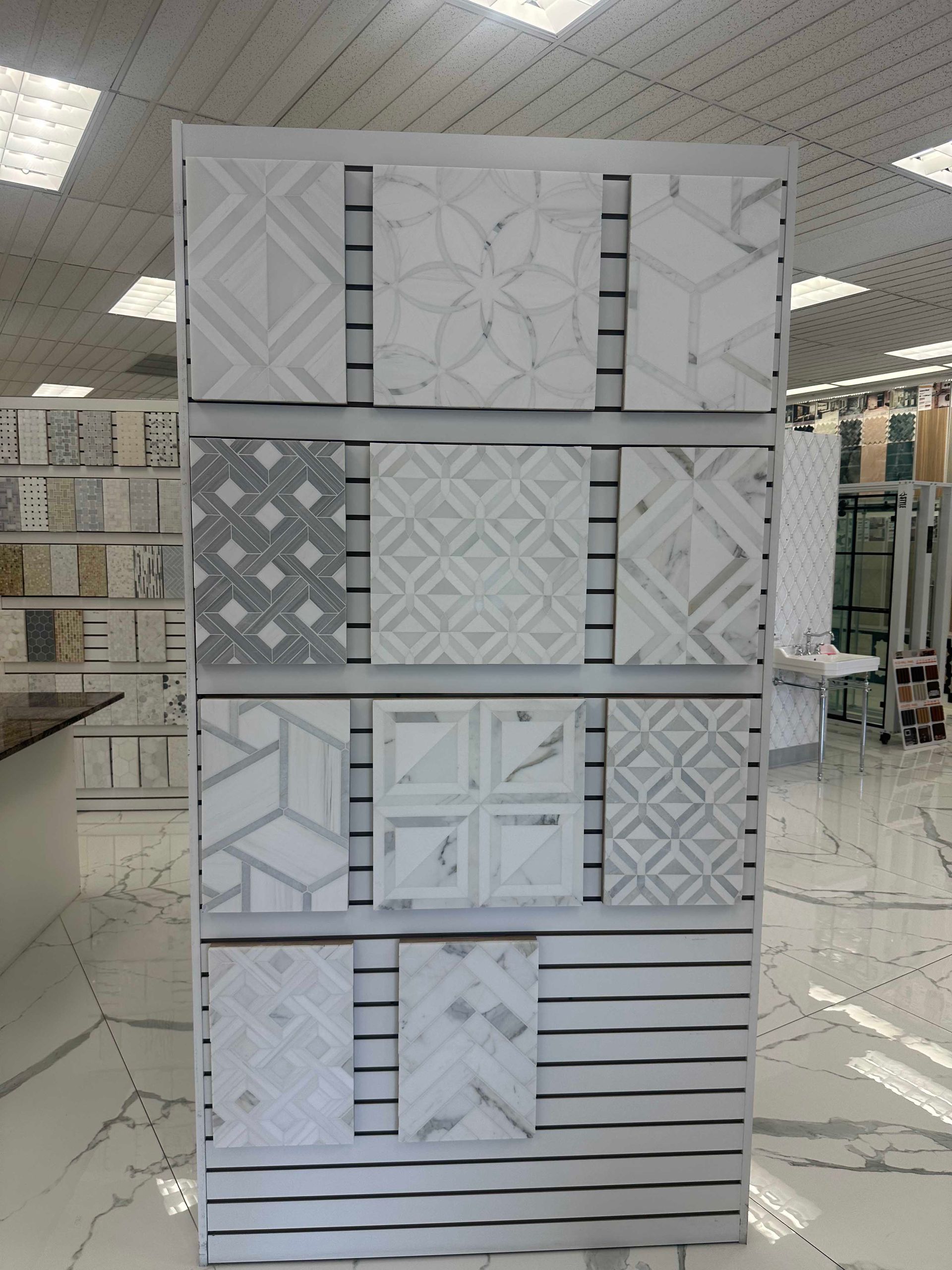 Display of various patterned white and gray tiles in a showroom setting.