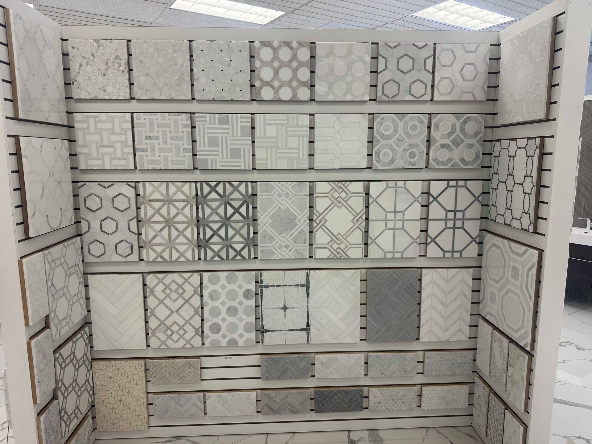 Display of various patterned ceramic tiles in shades of gray and white on a retail display.