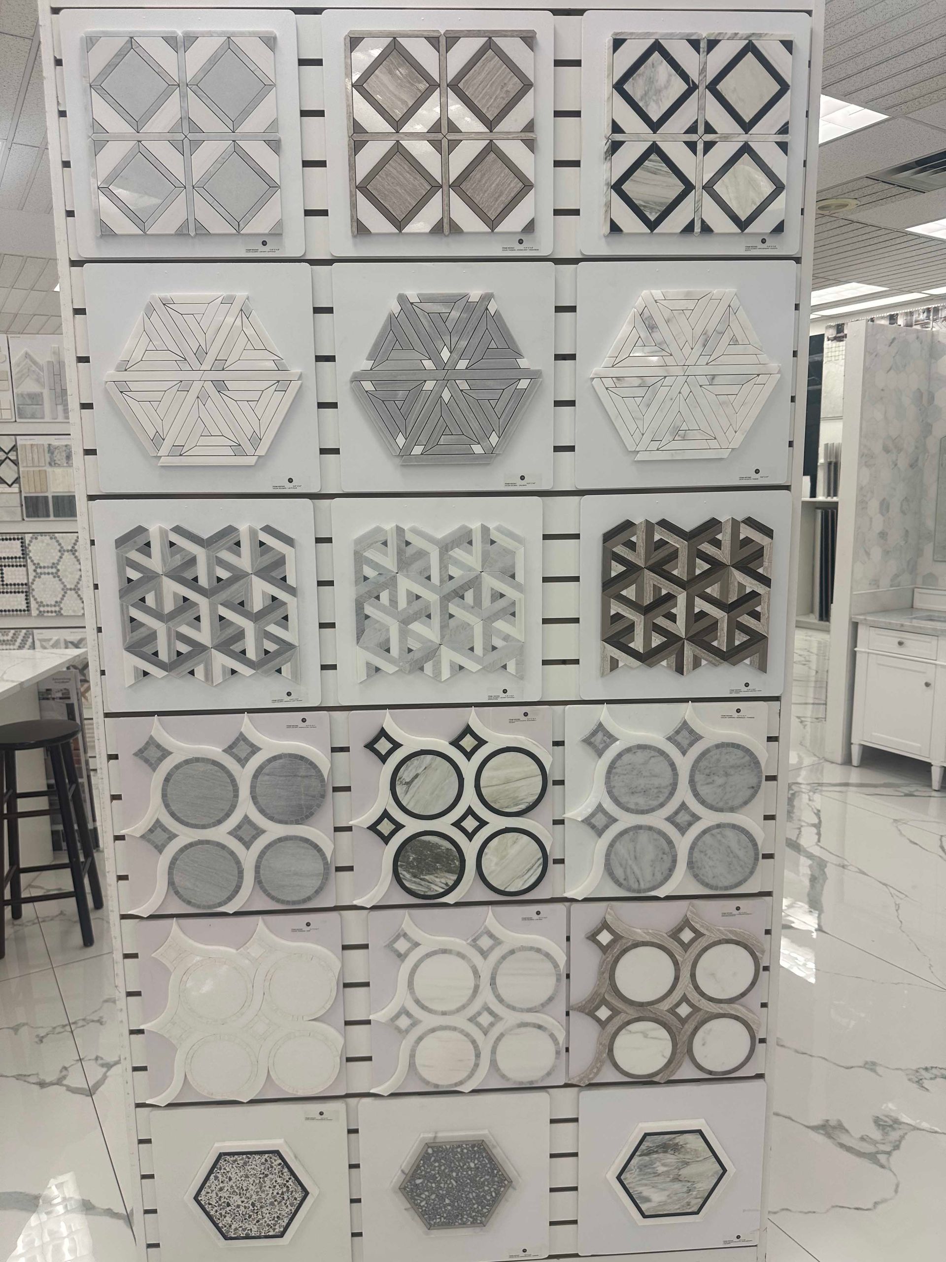 Display of various decorative tiles in a showroom, arranged on a white vertical panel.