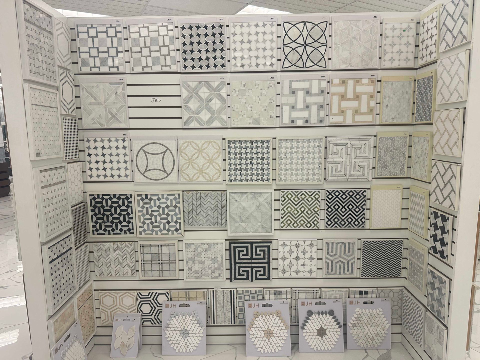Display of patterned tiles in various grayscale designs, arranged on shelves.