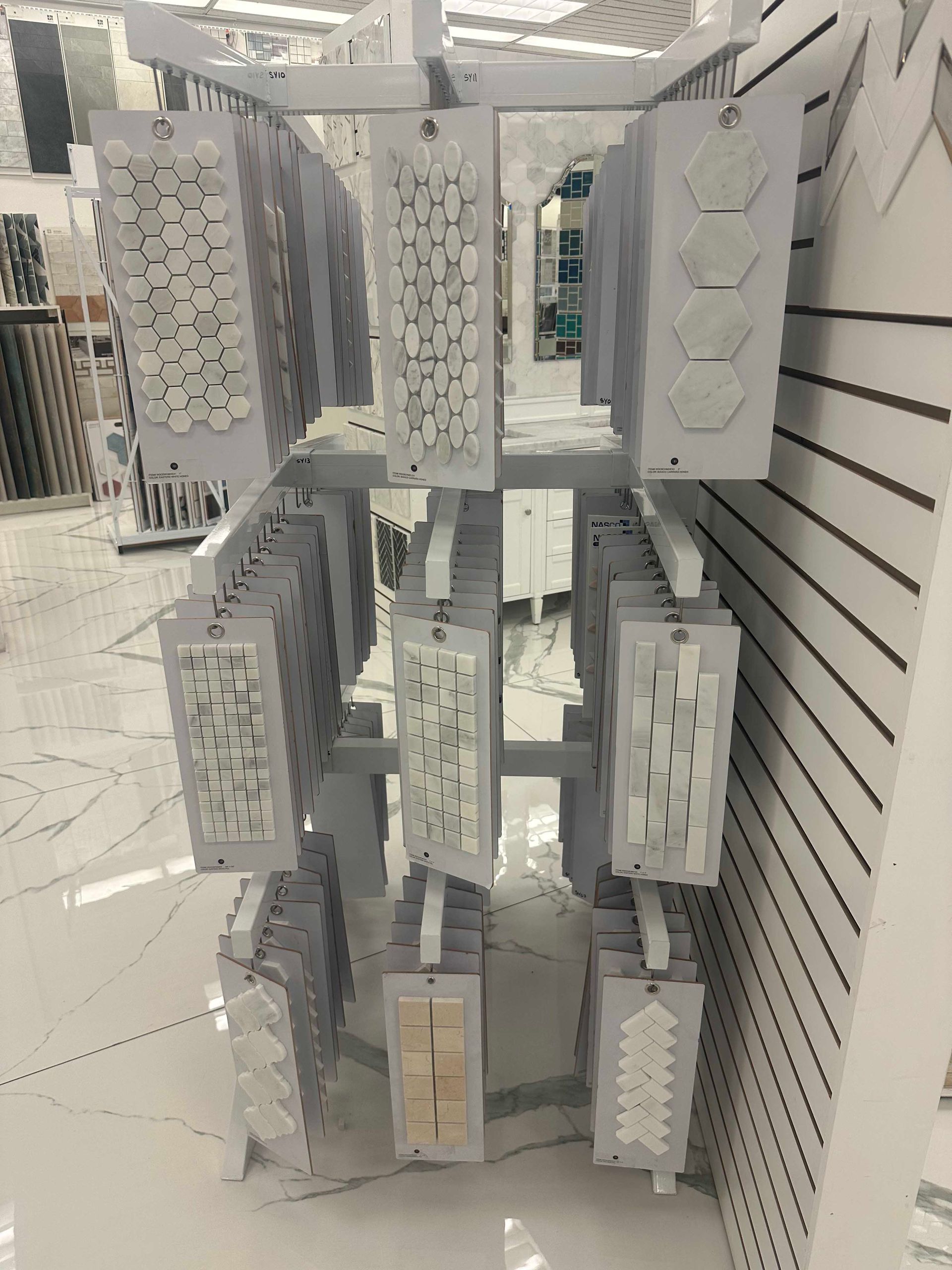 Tile samples displayed on a metal rack in a store. White, gray, and beige colors are visible.